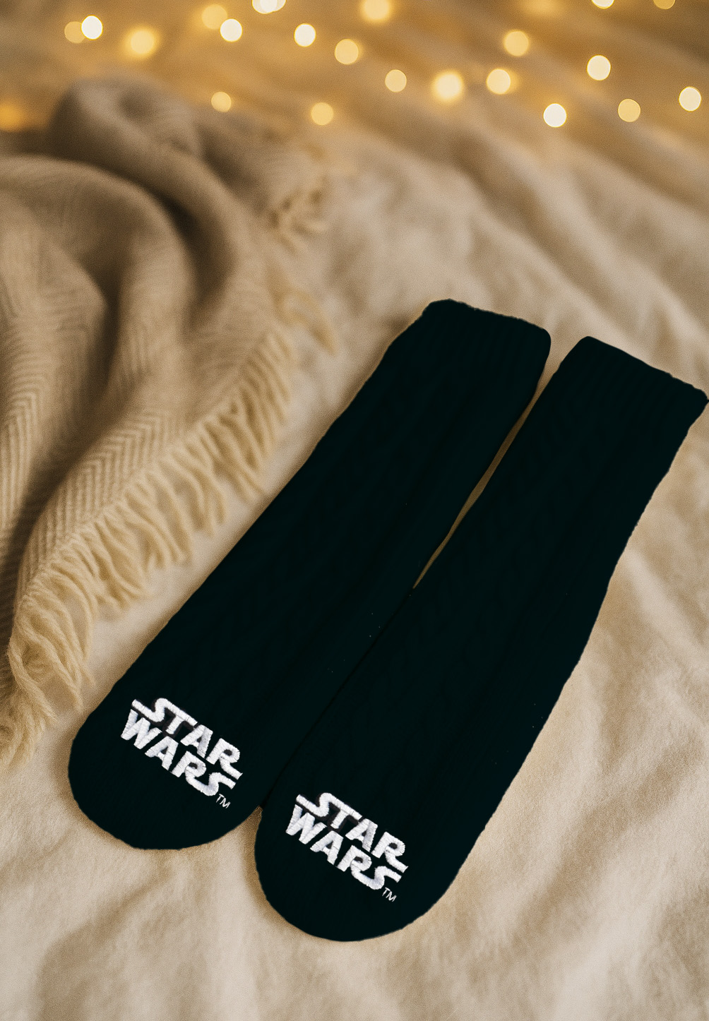 Zwei schwarze Socken mit Star Wars Logo liegen auf einer Decke.