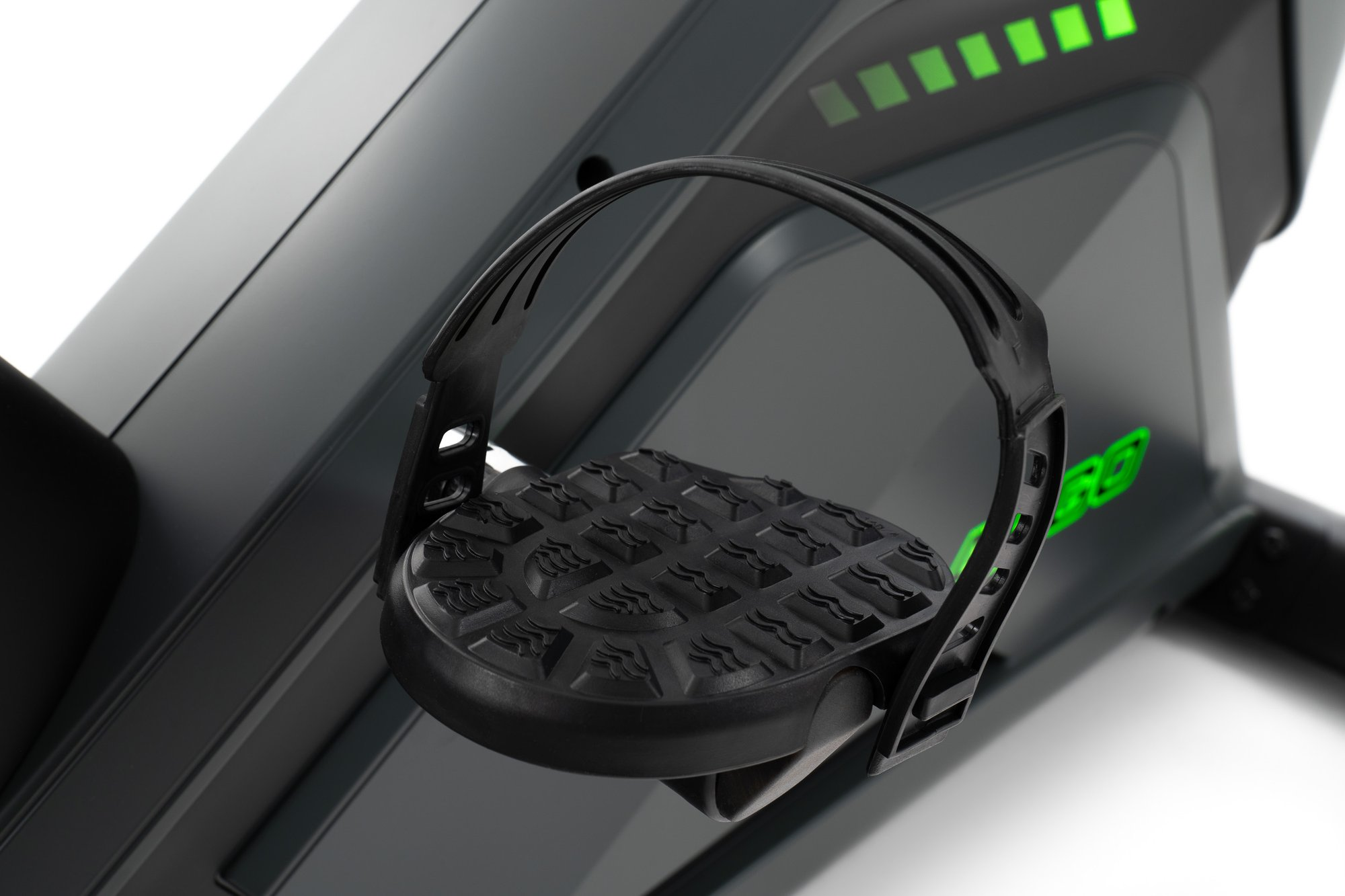 Nahaufnahme eines schwarzen Fahrradpedals mit Riemen und Gummigriff. Grüne Lichter im Hintergrund.