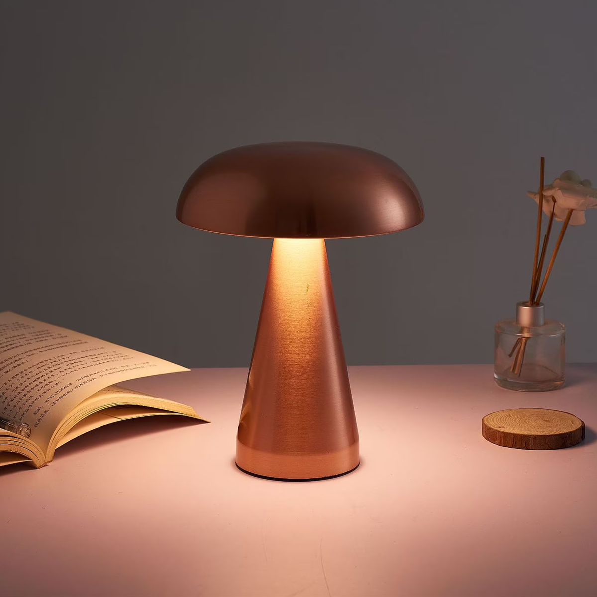 Eine kupferfarbene Pilzlampe leuchtet auf einem Schreibtisch neben einem Buch und einem Diffusor.