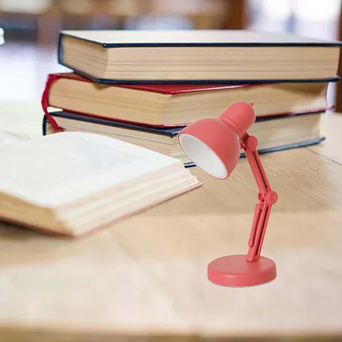 Ein kleiner, roter Schreibtischlampenarm steht neben gestapelten Büchern.