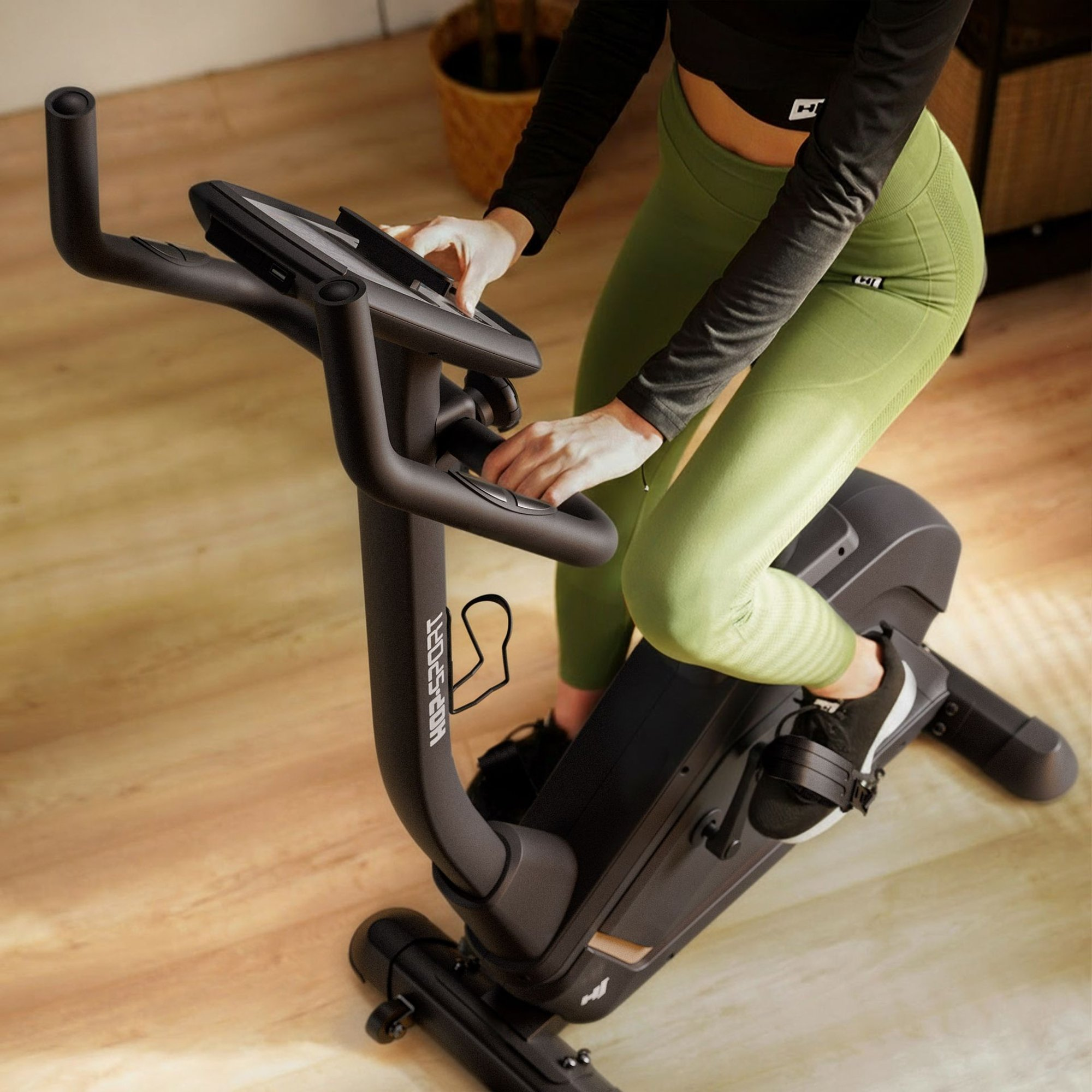 Eine Person in Trainingskleidung fährt auf einem schwarzen Heimtrainer auf einem Holzboden.