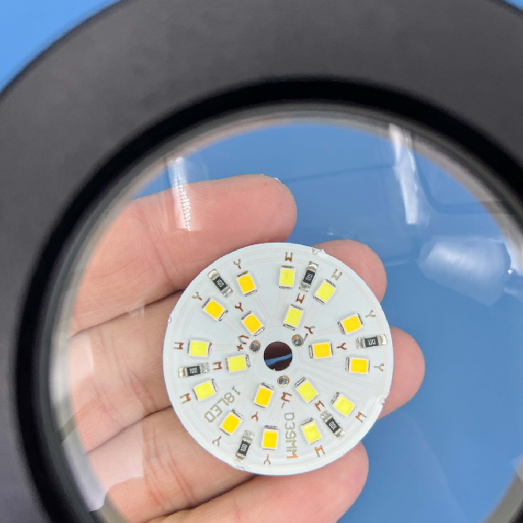 Eine Hand hält eine runde Platine mit LEDs, beleuchtet von einer Lupe.