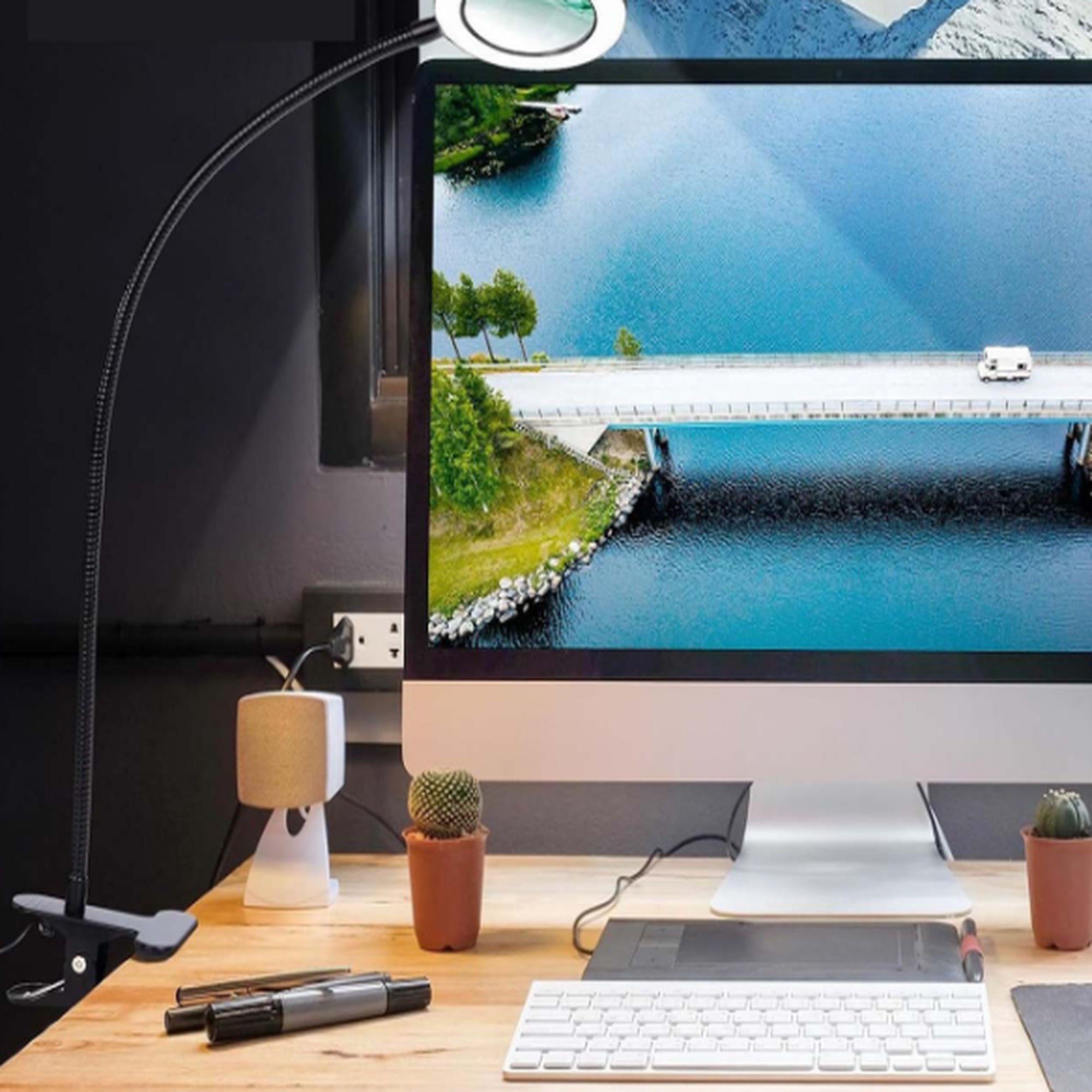 Schreibtisch mit Monitor, Tastatur, Stiften und einer Klemmleuchte mit Lupe.