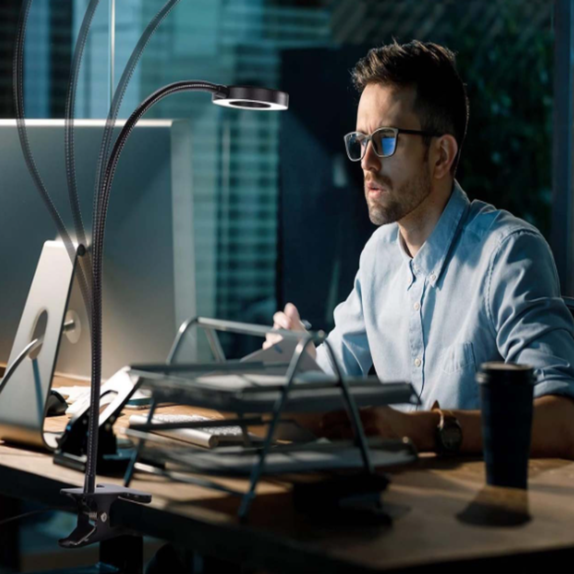 Ein Mann mit Brille arbeitet am Schreibtisch mit einem Computer und einer Schreibtischlampe.