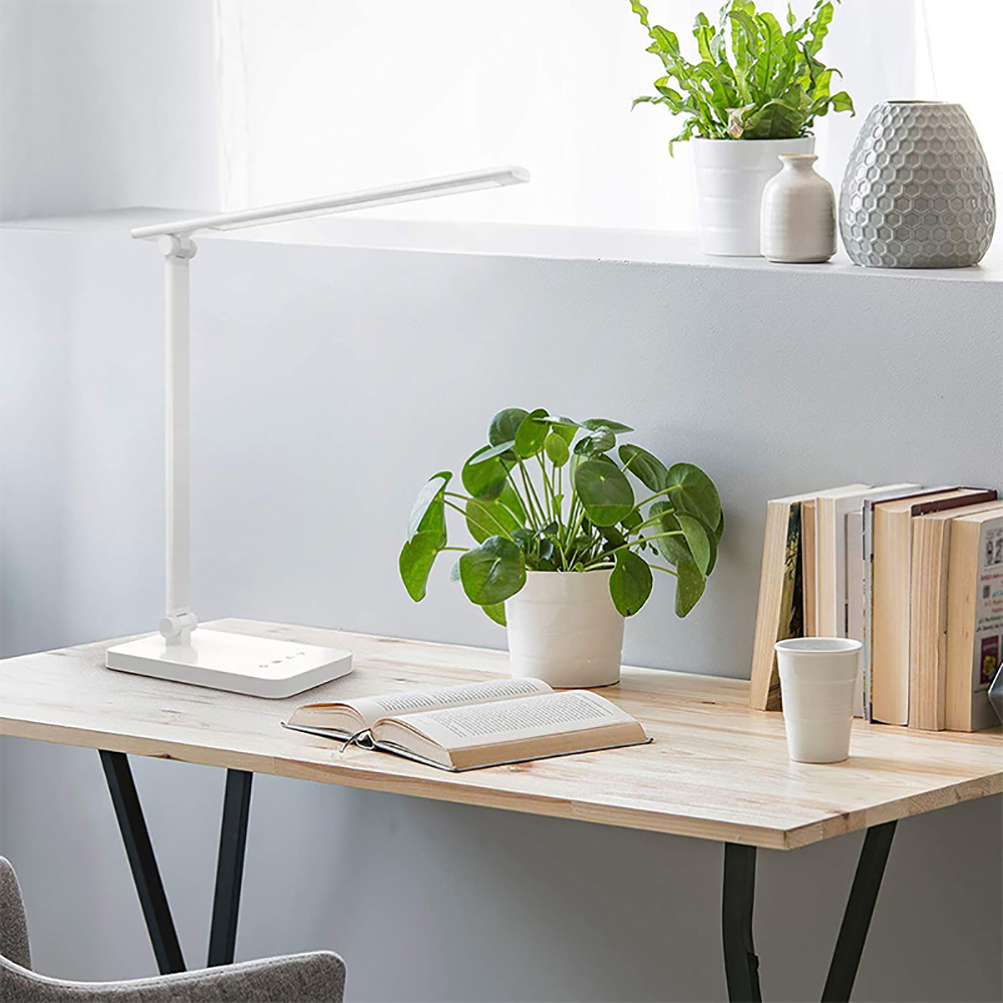 Ein weißer Schreibtisch mit Lampe, Buch und Topfpflanzen.
