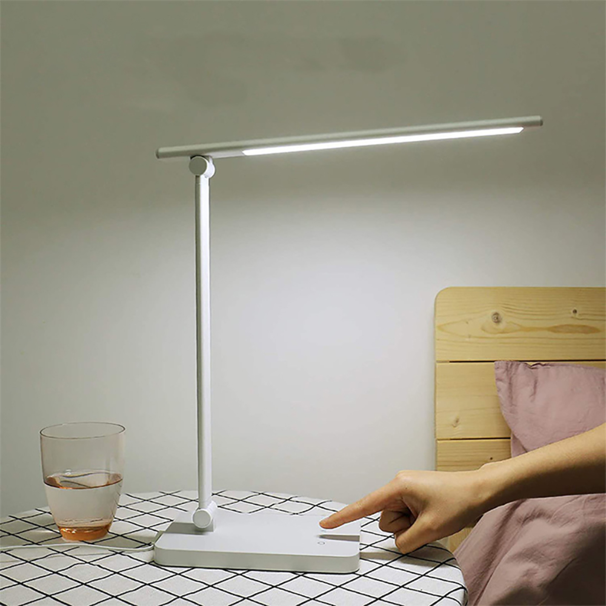 Eine weiße Schreibtischlampe leuchtet auf einem Tisch neben einem Glas Wasser.