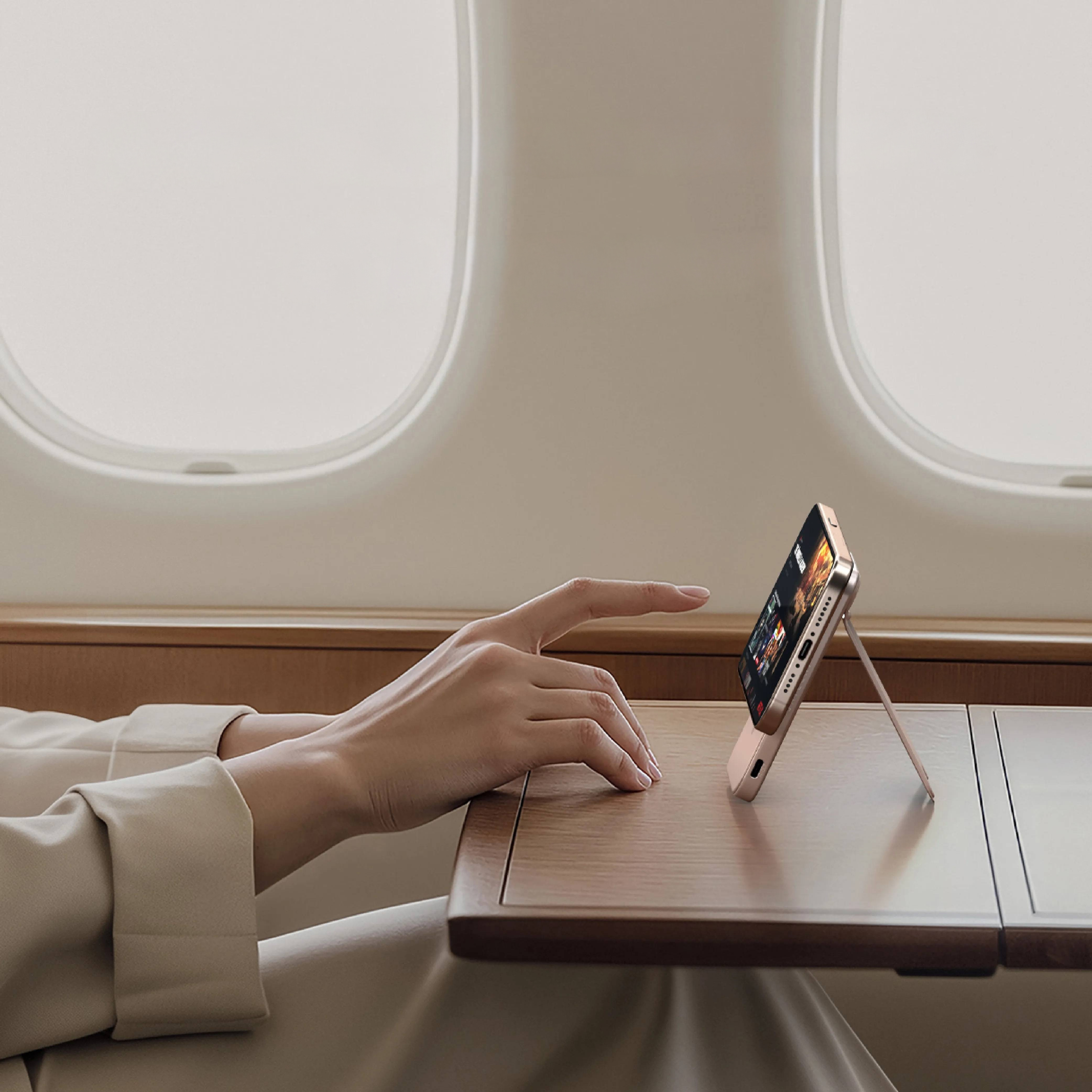 Eine Hand ruht auf einem Tisch neben einem Handy auf einem Ständer in einem Flugzeug.