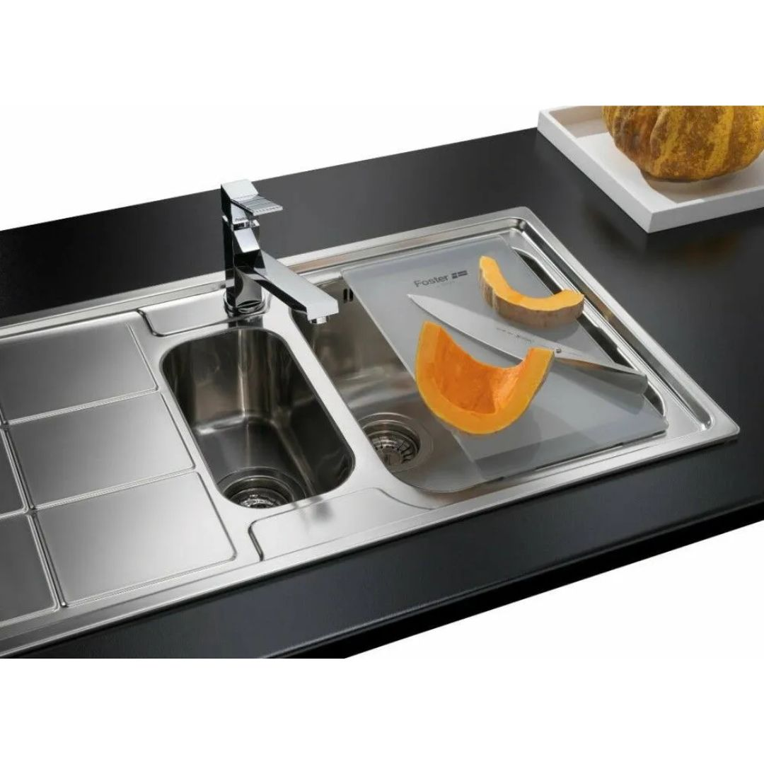 Un lavello da cucina in acciaio inossidabile con rubinetto, tagliere e pezzi di zucca.
