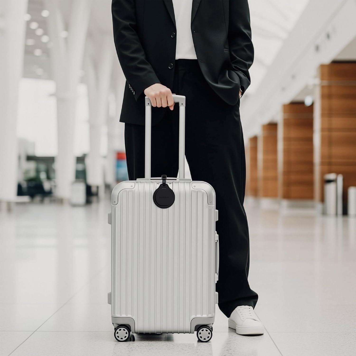 Person im schwarzen Anzug mit silbernem Koffer am Flughafen.