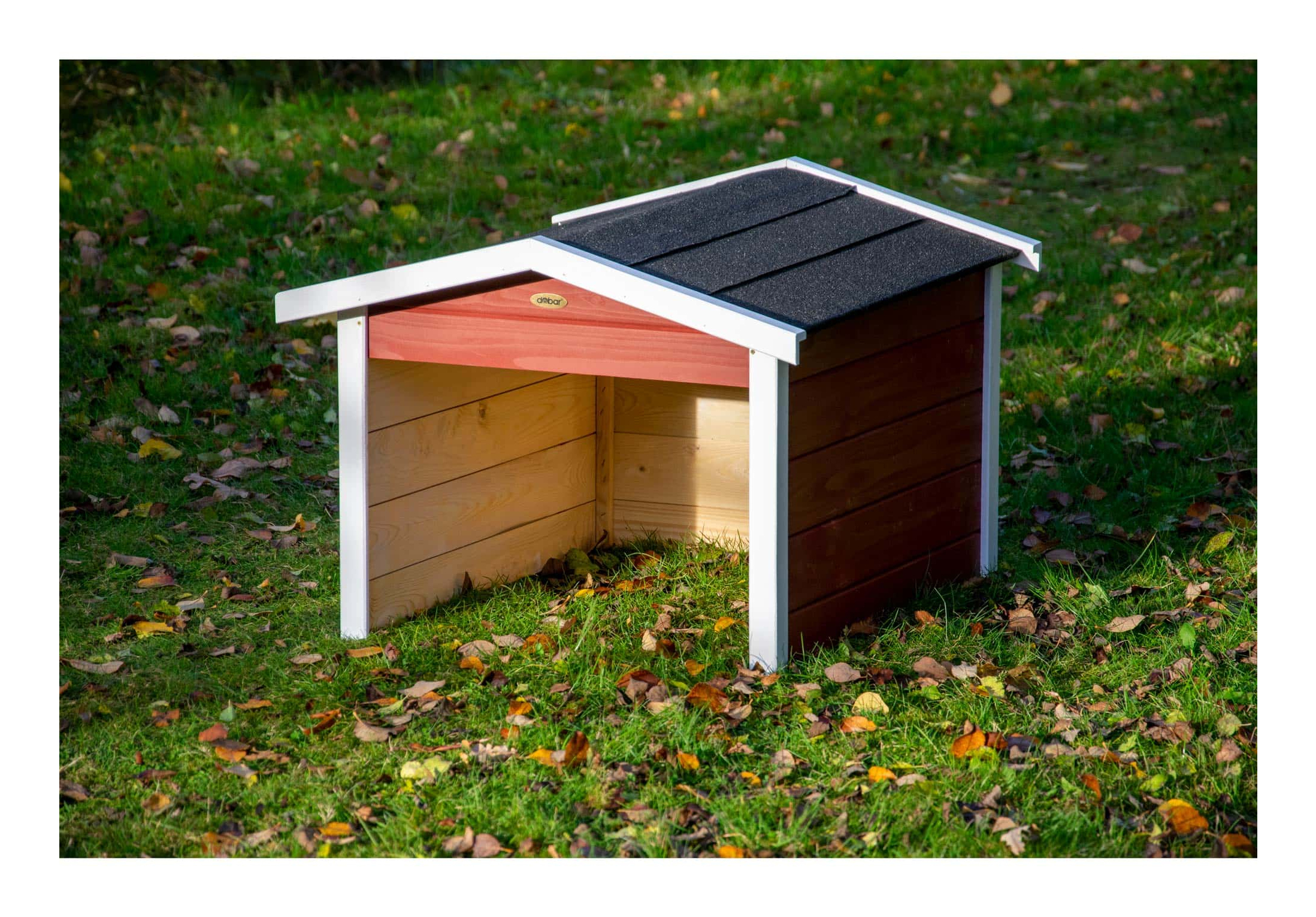 Ein hölzernes Hundehaus steht auf grasbewachsenem Boden mit Blättern.