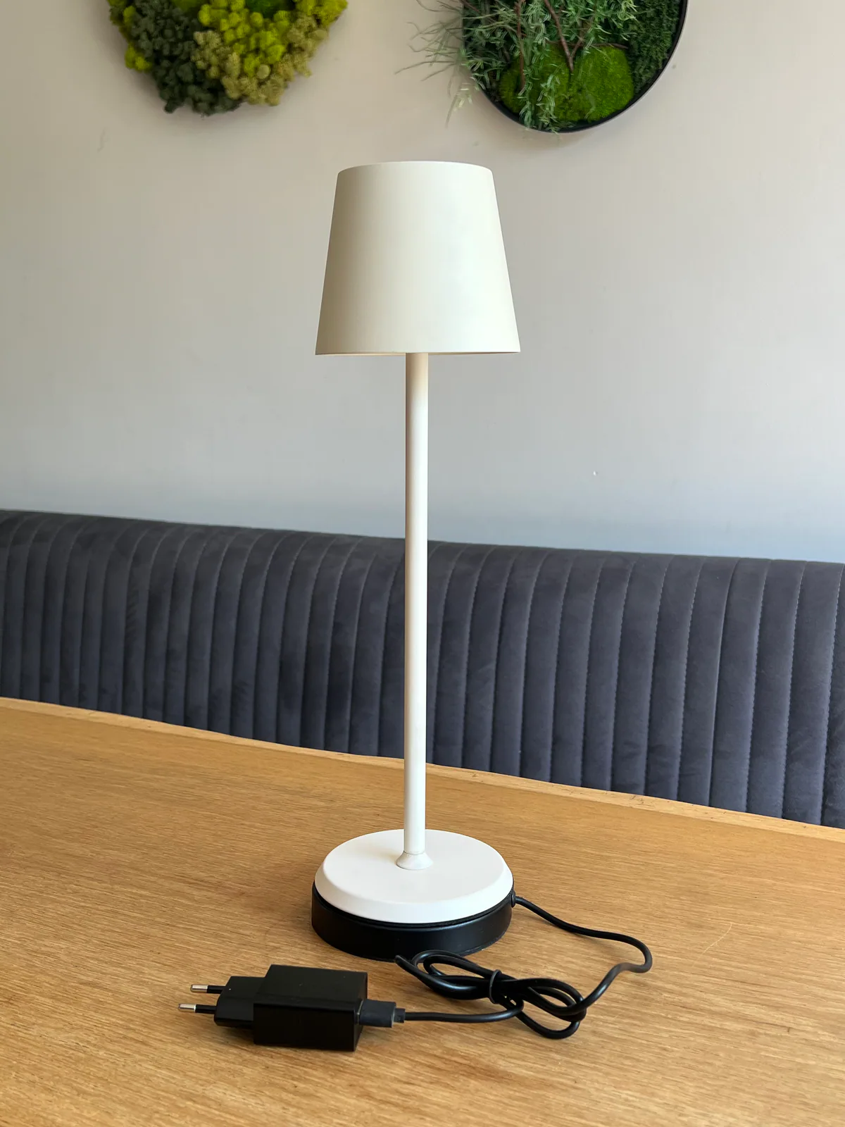 Eine weiße Tischlampe mit schwarzem Sockel und Kabel auf einem Holztisch.