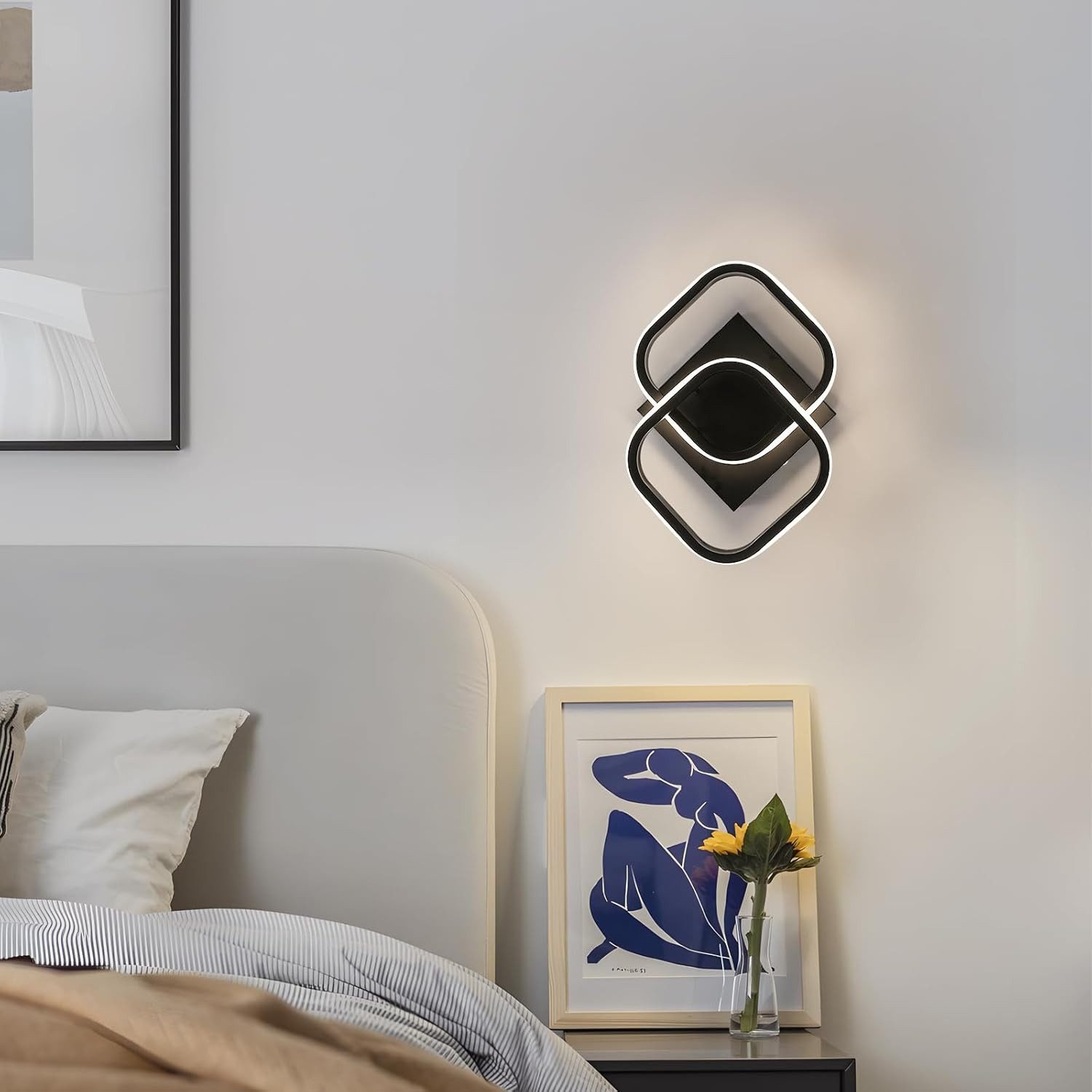 Moderne Wandleuchte mit geometrischem Design über gerahmtem Kunstwerk und Bett.