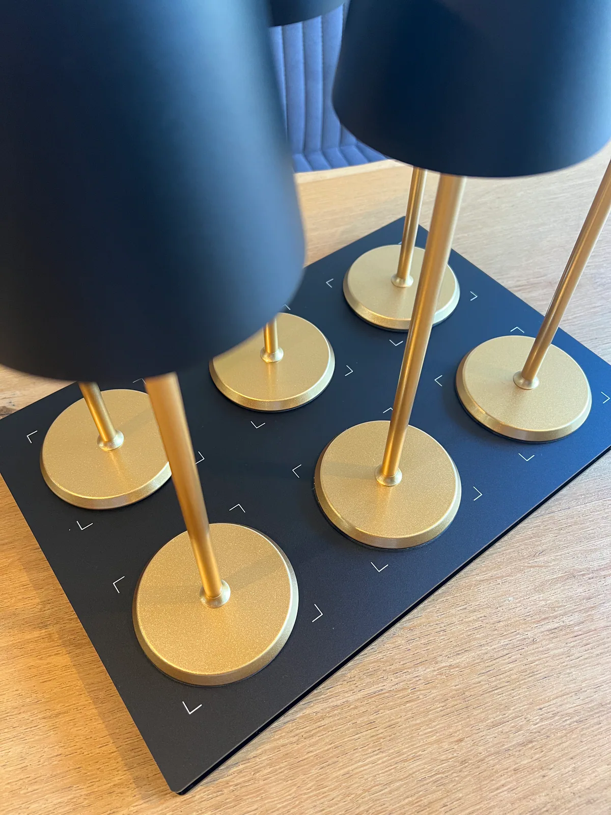 Sechs Lampen mit schwarzen Schirmen und goldenen Stielen auf schwarzer Basis.