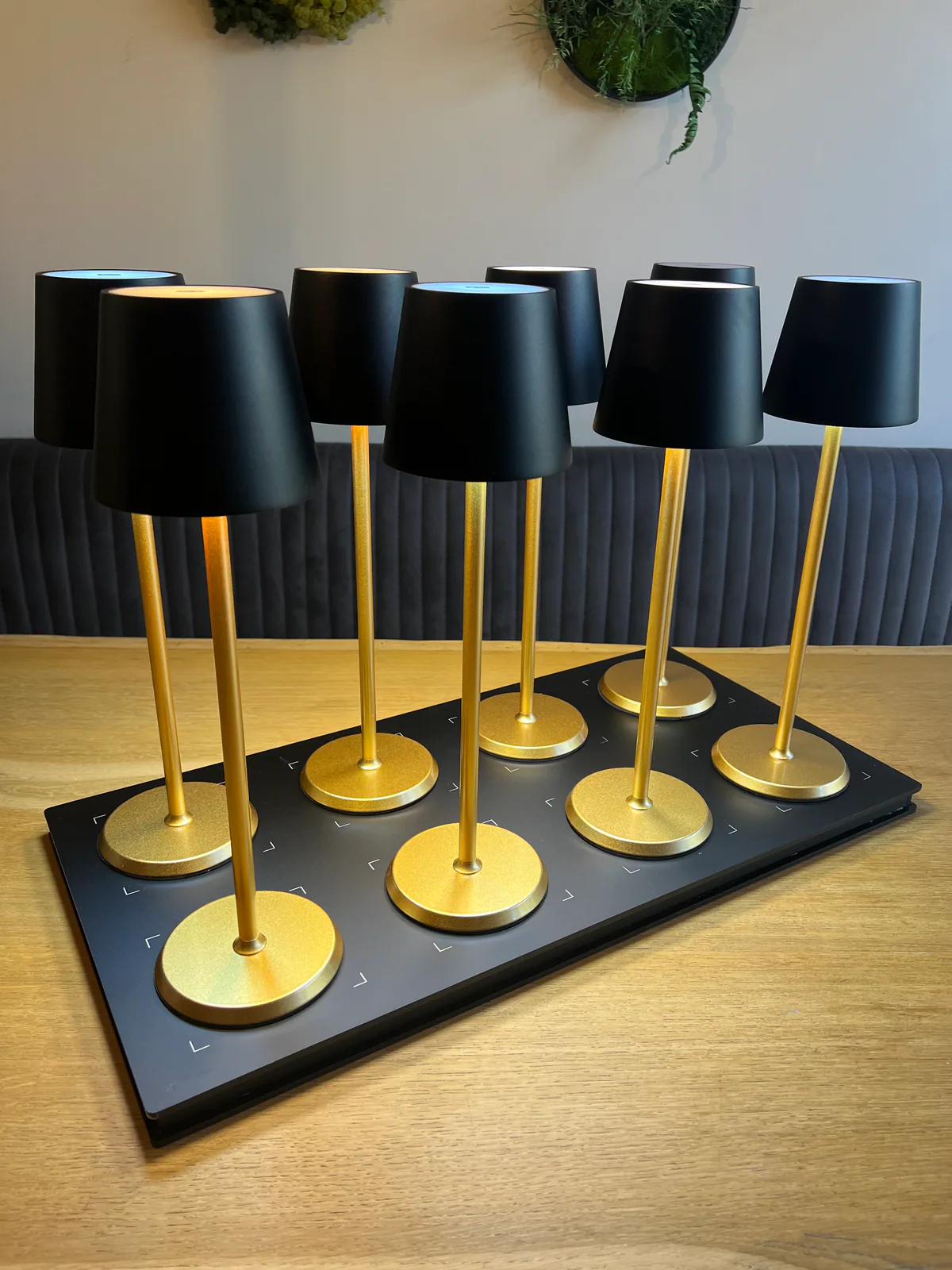 Neun schwarze Tischlampen mit goldenen Ständern auf einer schwarzen Ladeplatte.