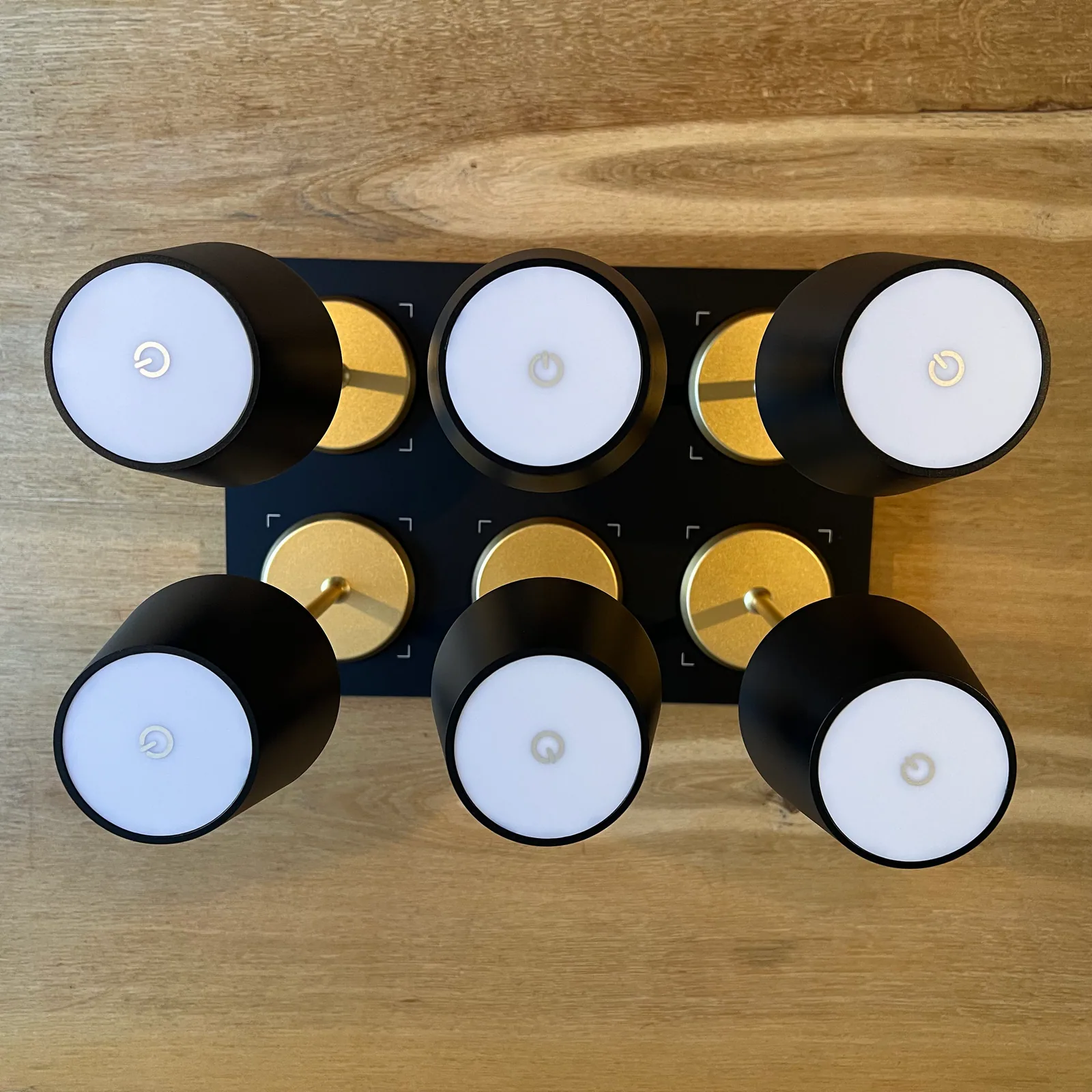 Sechs schwarze Leuchten mit weißer Mitte und goldenen Akzenten auf Holz.