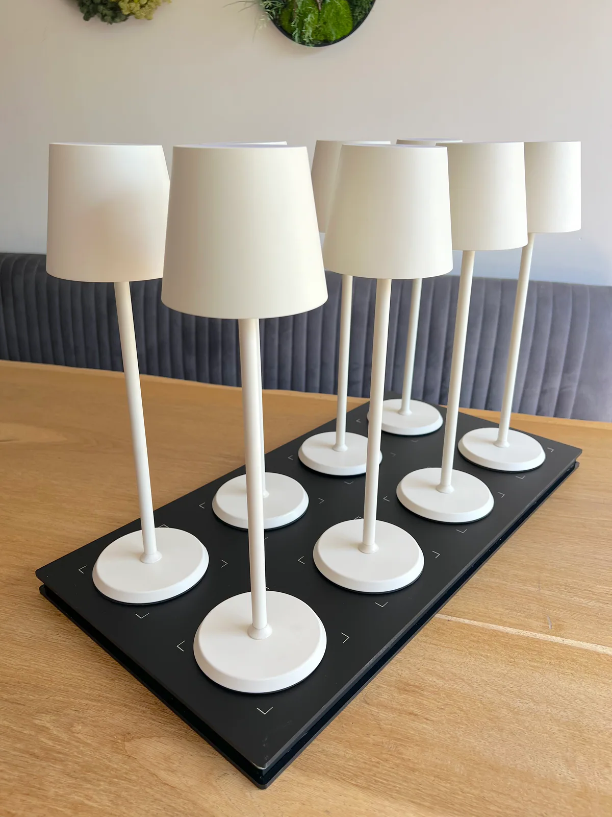 Sechs weiße Tischlampen stehen auf einer schwarzen Ladeplatte.