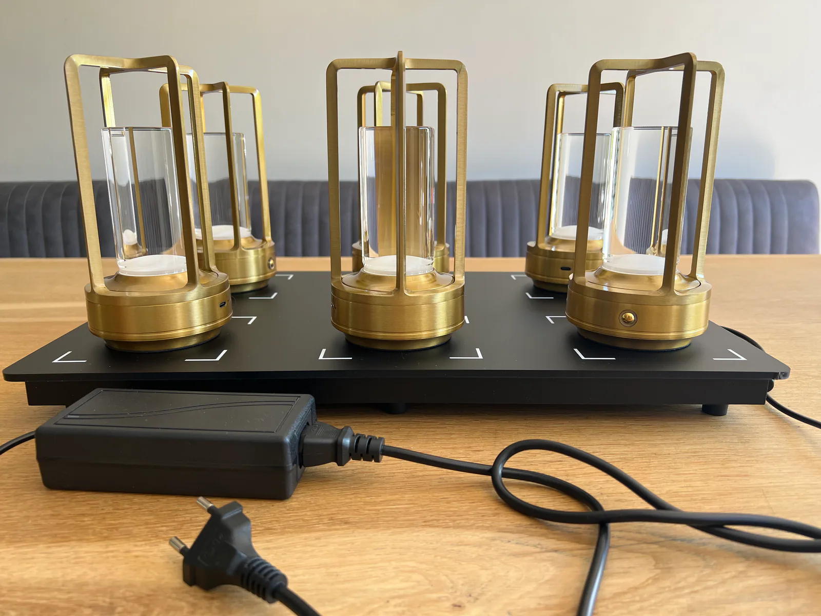 Sechs goldene Kerzenhalter mit Glaszylindern auf einer schwarzen Basis mit Netzteil.