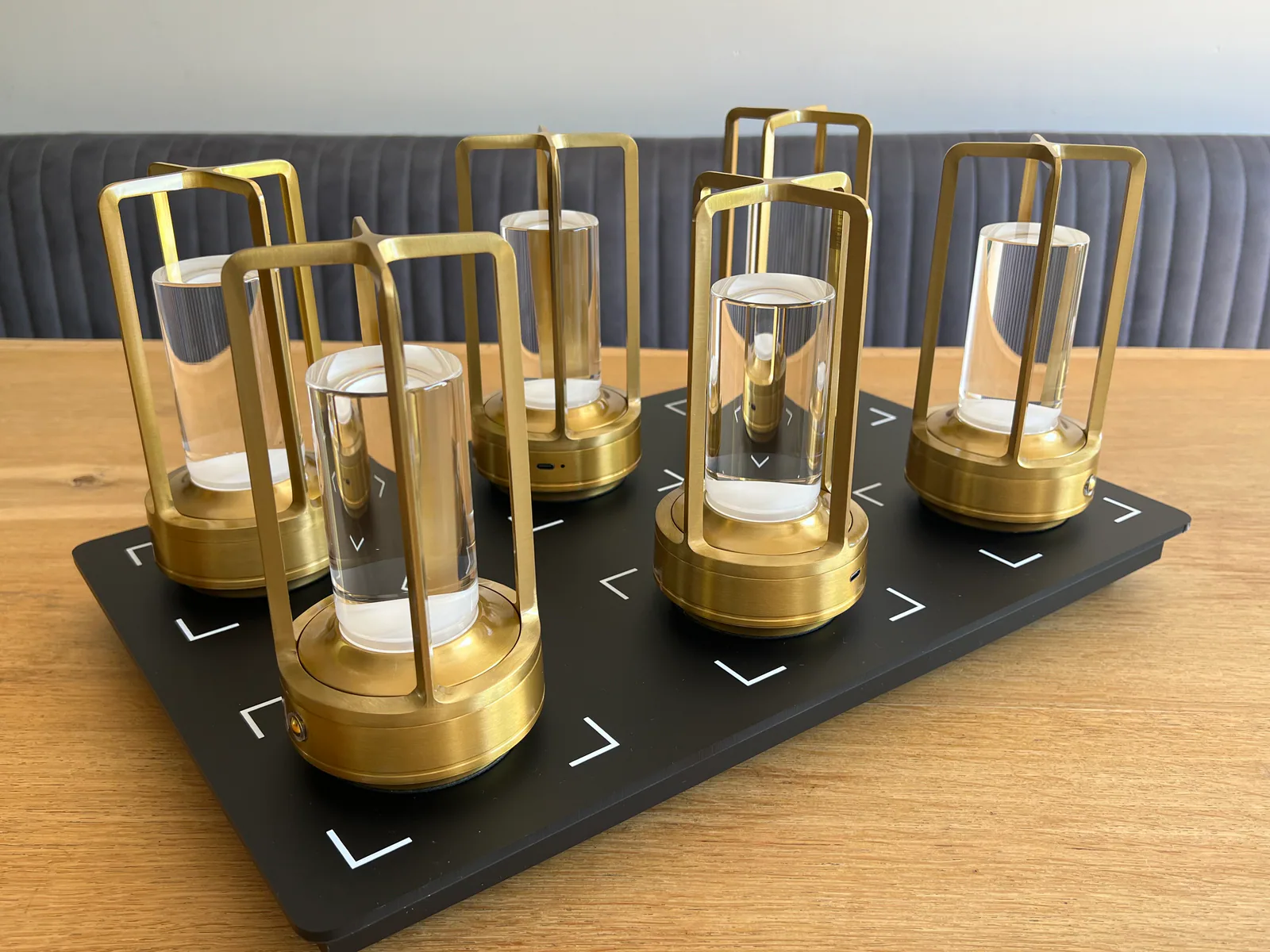 Sechs goldene Laternen mit Glaszylindern stehen auf einer schwarzen Platte.