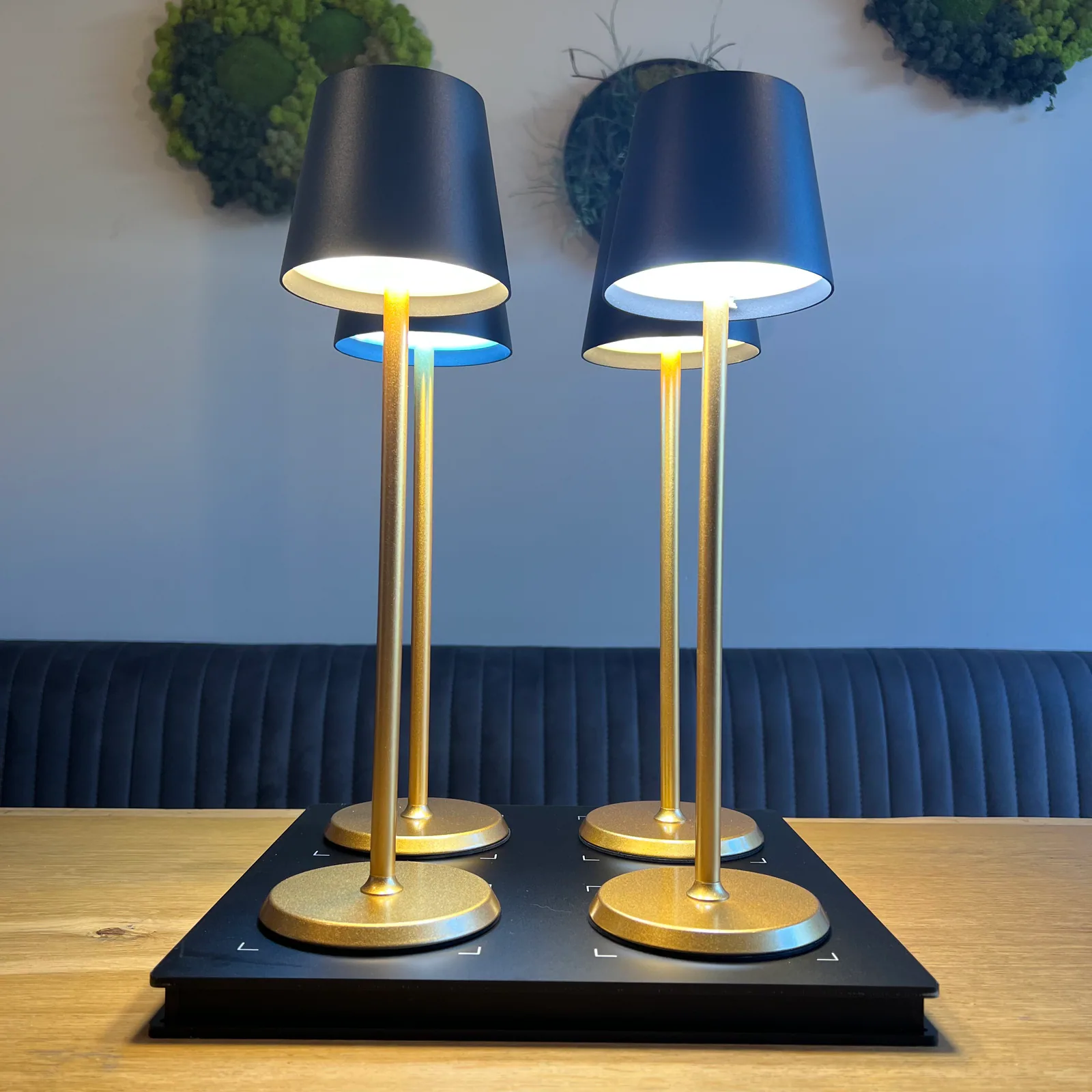 Vier goldene Tischlampen mit schwarzen Schirmen auf einem schwarzen Ladegerät.