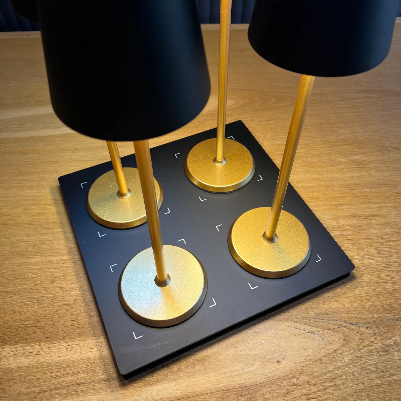 Vier Lampen mit schwarzen Schirmen und goldenen Ständern auf schwarzer Basis.