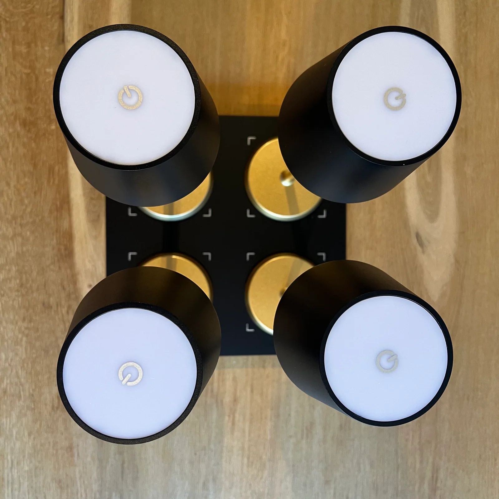 Vier schwarze Lampen mit weißen Lichtern und goldenen Akzenten auf Holz.