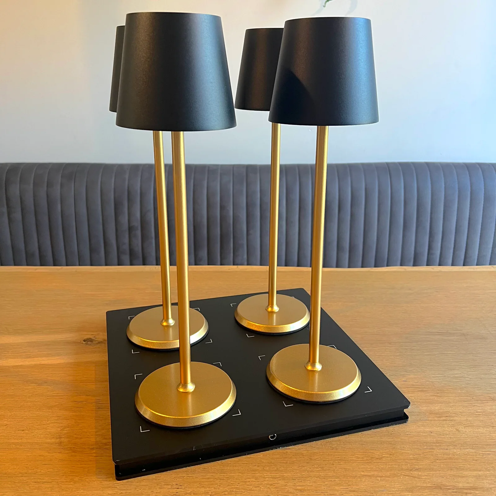 Vier goldene Tischlampen mit schwarzen Schirmen auf einer Ladeplatte.