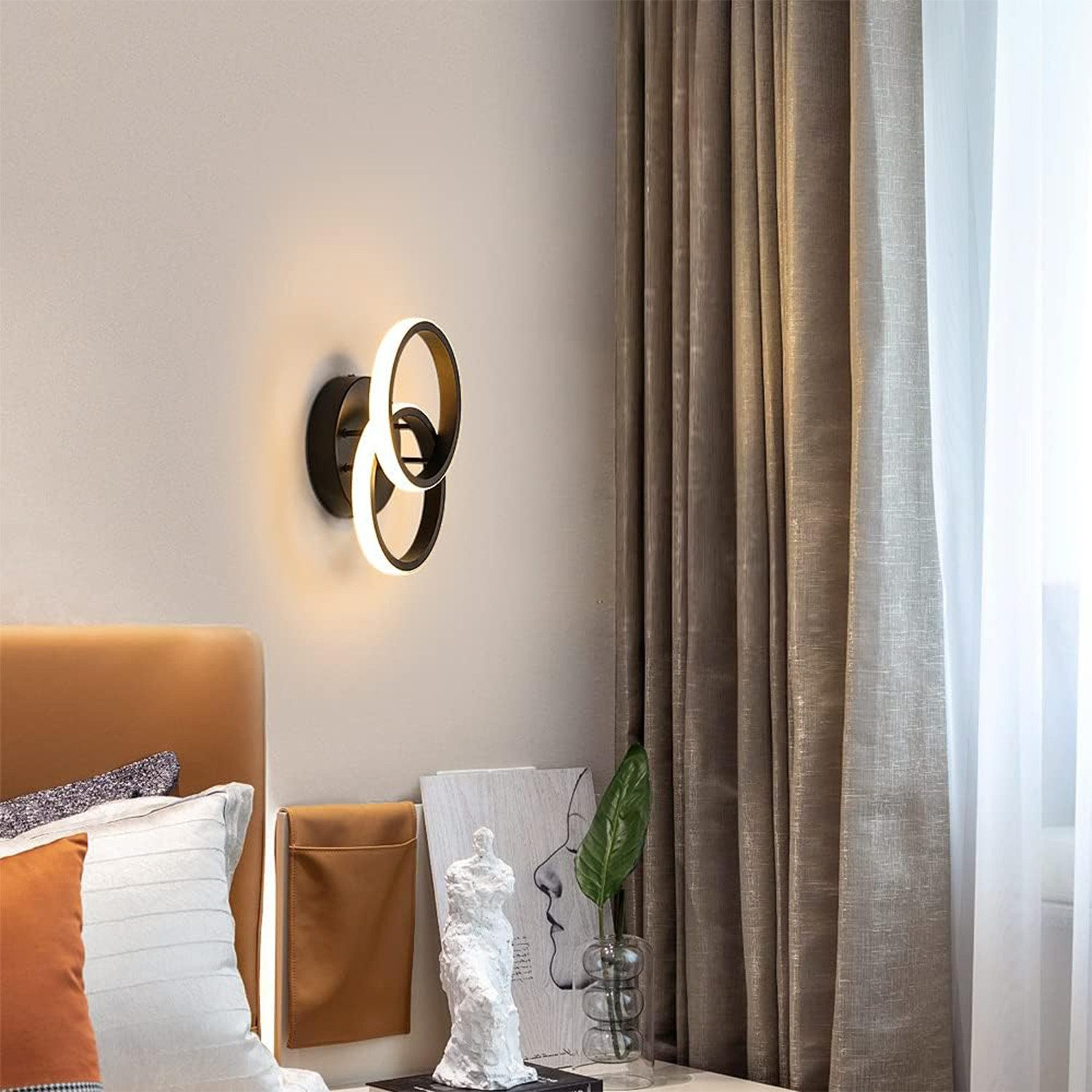 Moderne Wandleuchte mit zwei ineinandergreifenden Ringen, wirft warmes Licht auf ein Nachttisch.