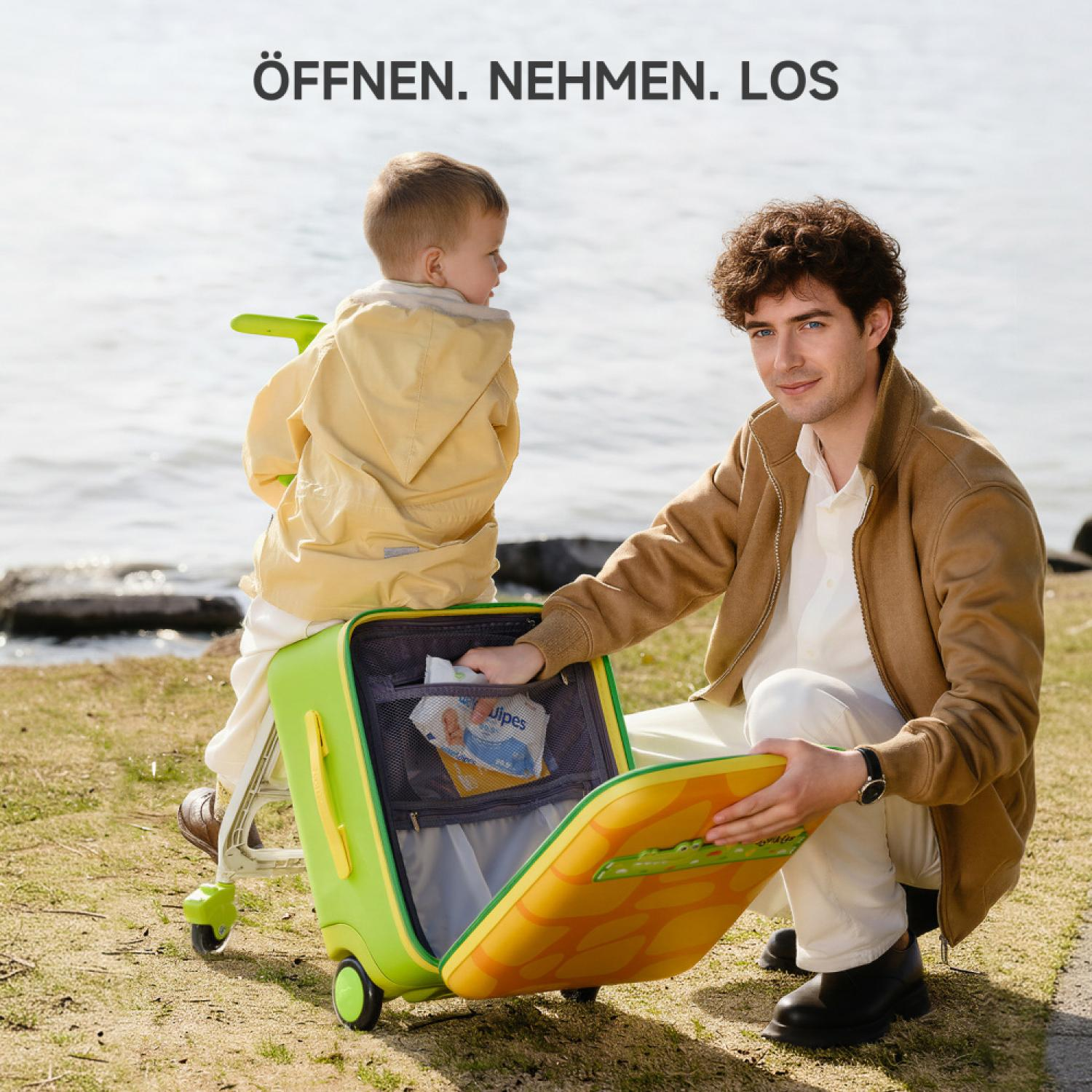 Mann und Kind packen einen grünen Koffer am Wasser.