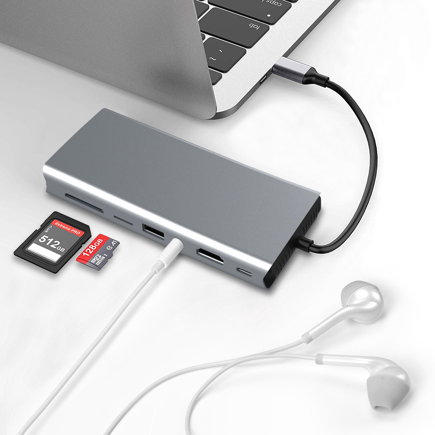 Silberne USB-C-Dockingstation an Laptop angeschlossen, SD-Karten und Ohrhörer daneben.