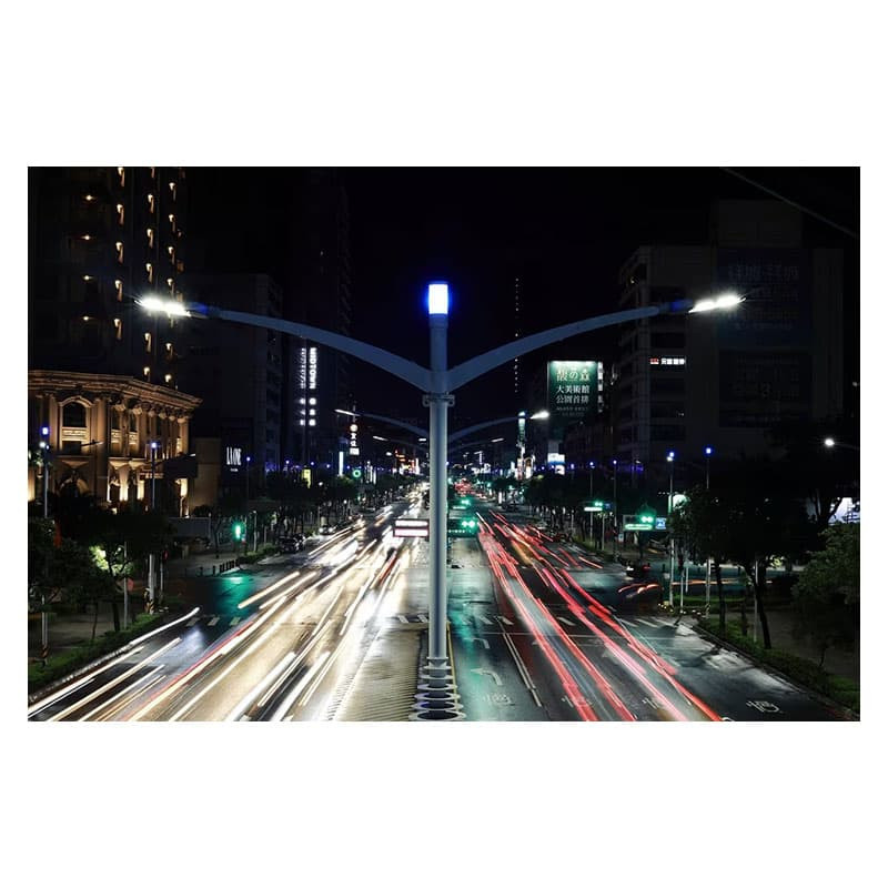 Scatto notturno a lunga esposizione di una strada trafficata con scie luminose di auto. Edifici e lampioni fiancheggiano la strada.