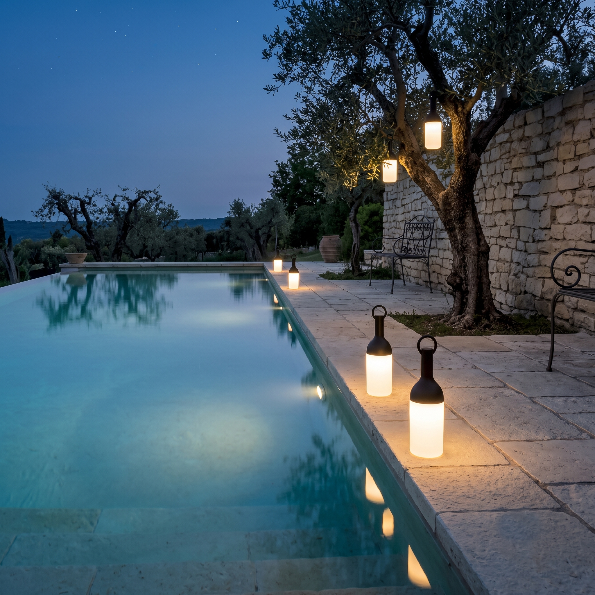 Ein Pool mit beleuchteten Laternen am Abend neben einem Steinwall und Bäumen.