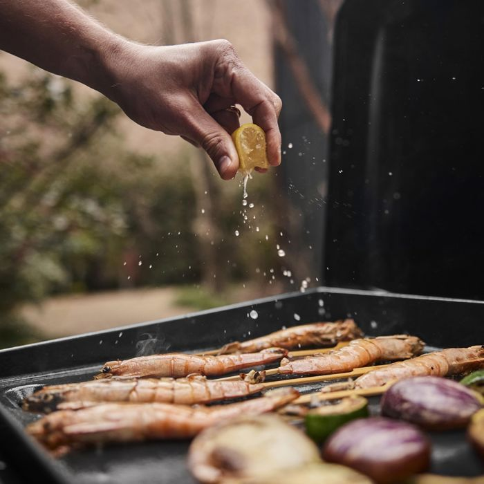 Hand perst citroen uit over garnalen en groenten op een grill. Buiten koken.