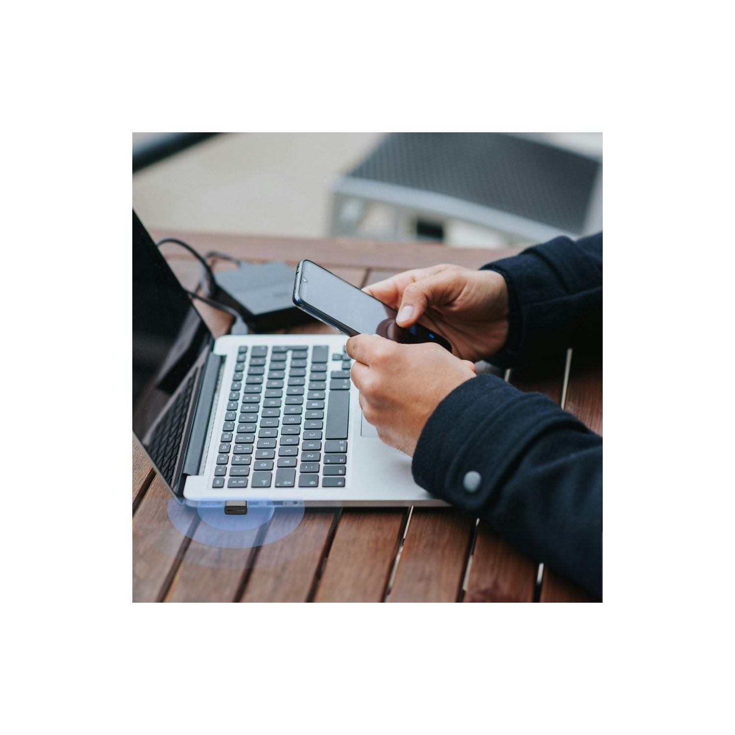 Ahşap masada laptop ve telefonlu adam, dizüstü bilgisayarda USB alıcısı.