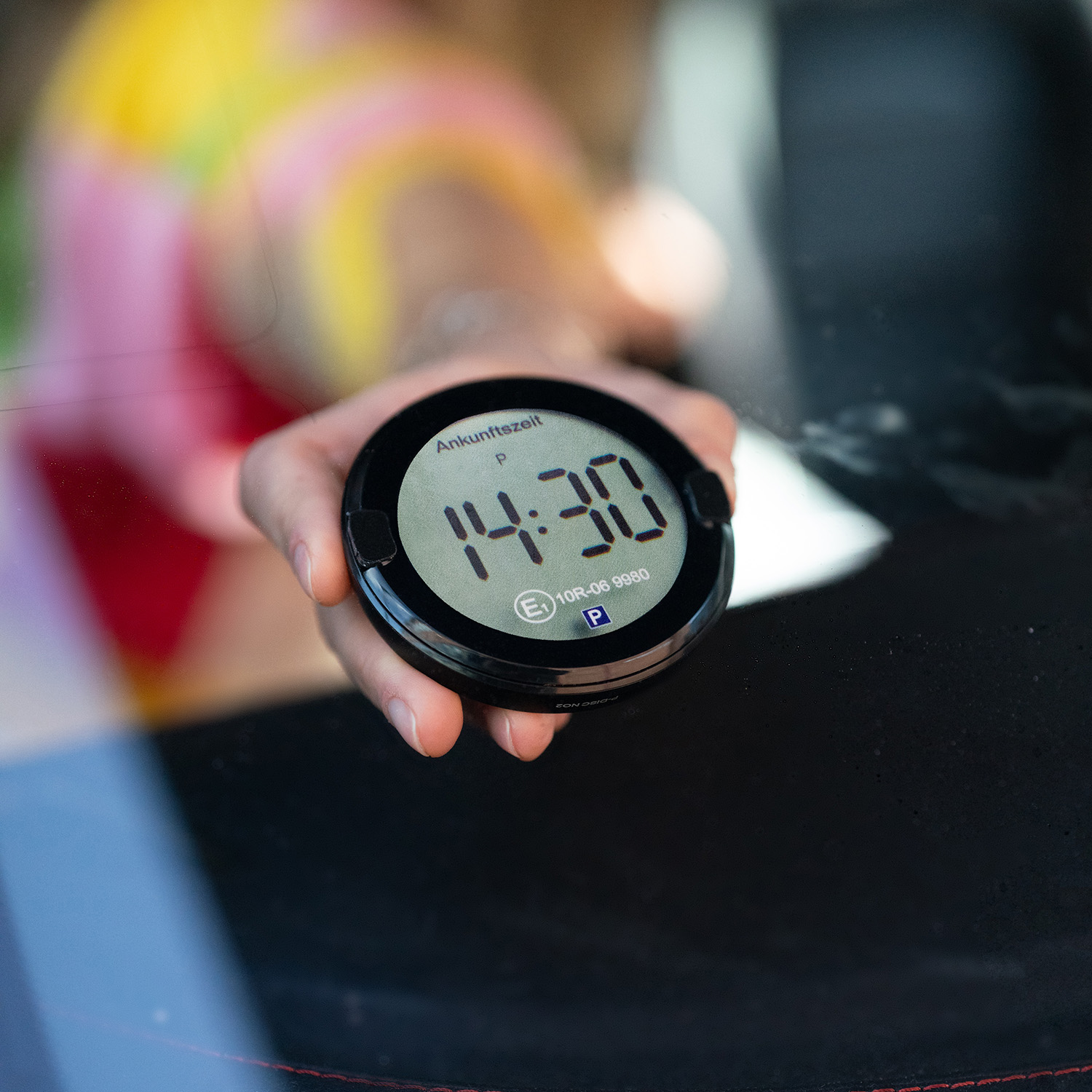 Eine Hand hält eine Parkscheibe mit der Anzeige 14:30.