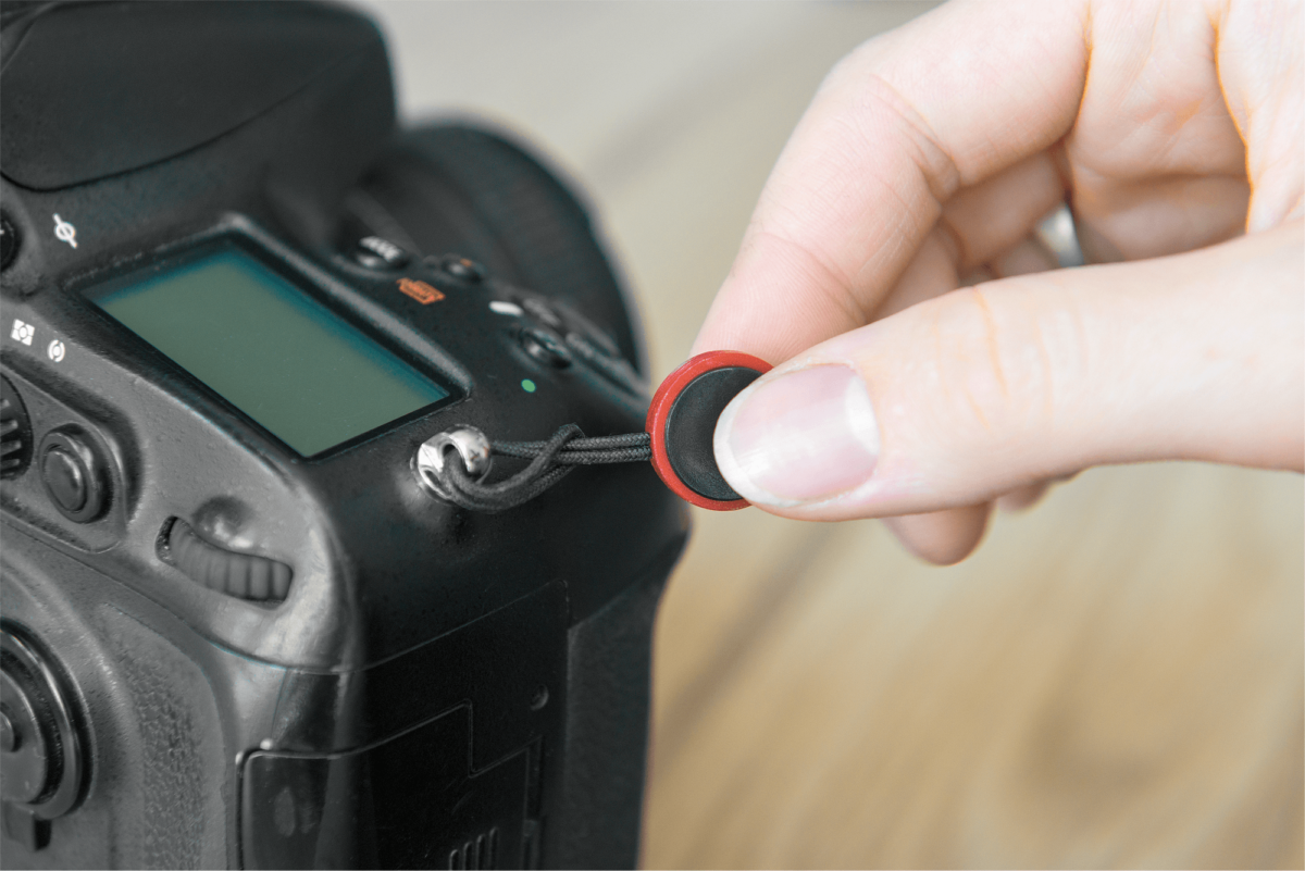 Una mano attacca un anello per cinghia della fotocamera rosso e nero a una fotocamera nera.