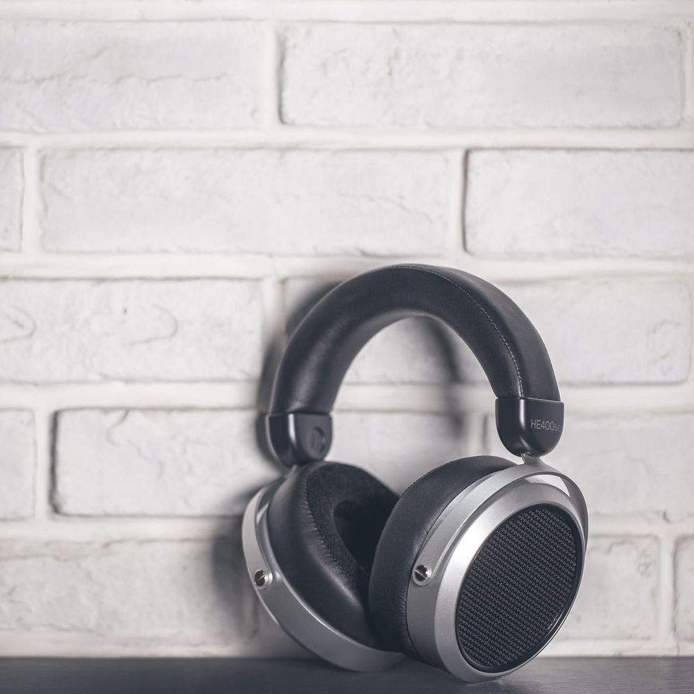 Auriculares negros circumaurales con detalles plateados descansan sobre una pared de ladrillos blancos.