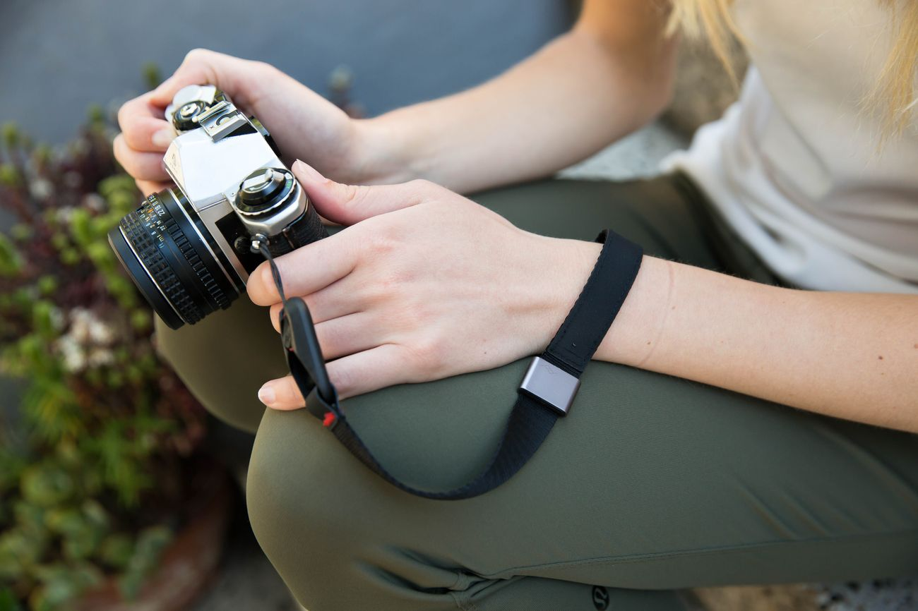 Una persona tiene una fotocamera d'argento con una cinghia nera.