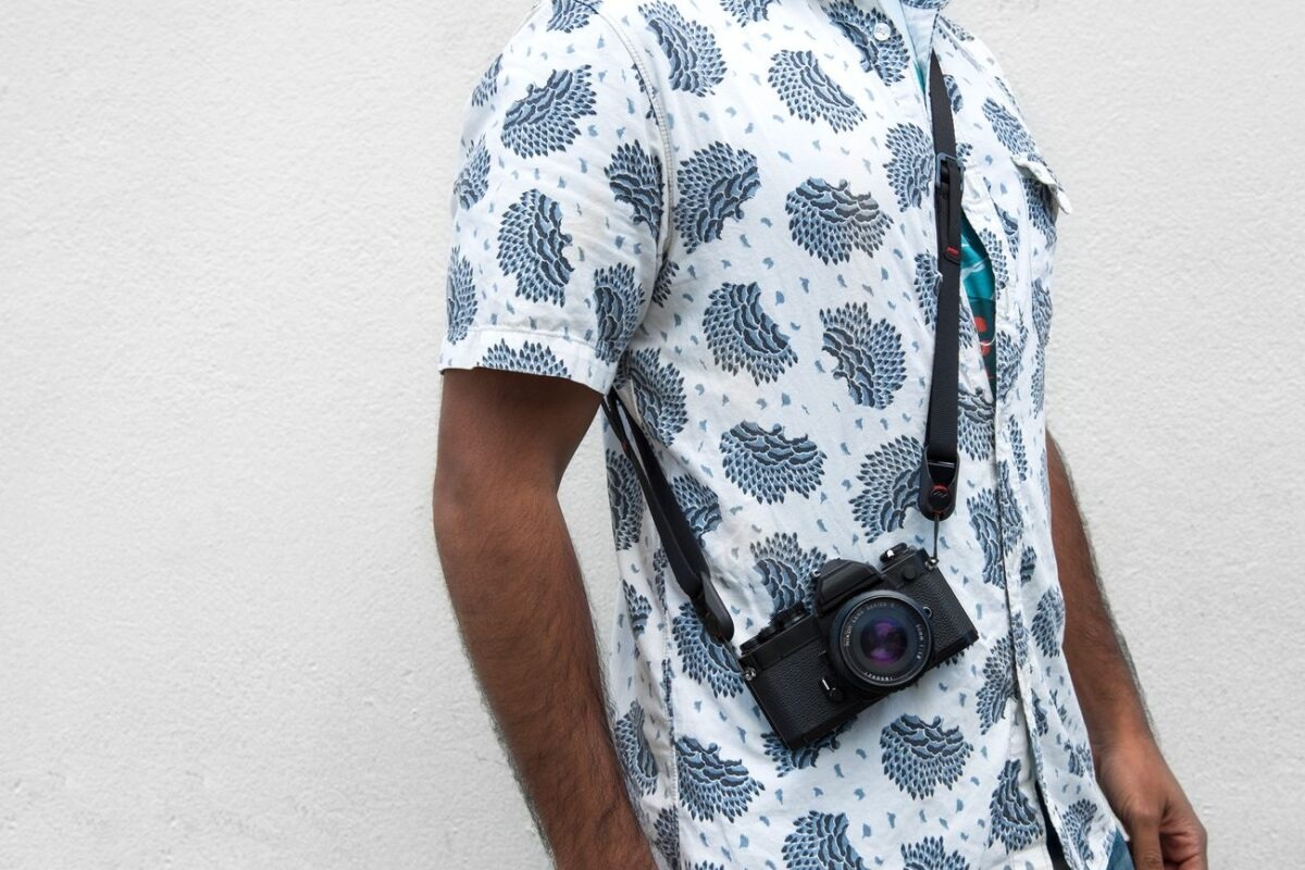 Uomo con camicia bianca a fantasia piuma blu, macchina fotografica nera al collo.