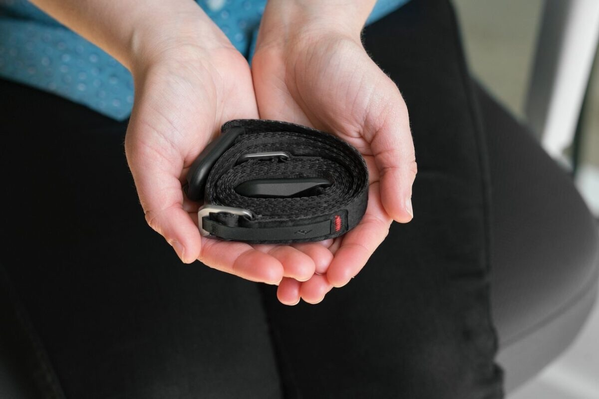 Mani tengono una cinghia nera arrotolata con fibbie argentate e clip nera.