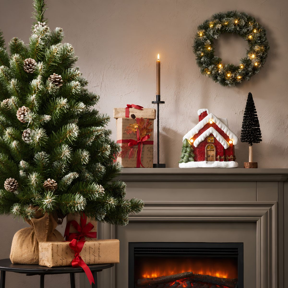 A festive fireplace mantel with a lit Christmas tree, gifts, a candle, wreath, and house decoration.
