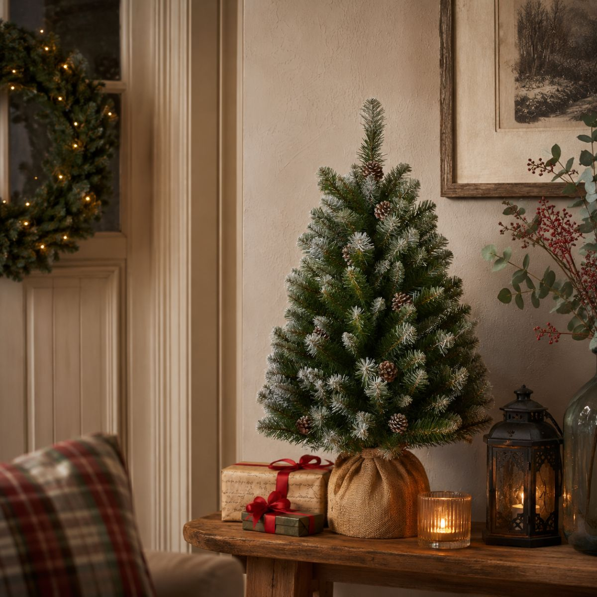 A small Christmas tree on a wooden table with gifts and a lantern.