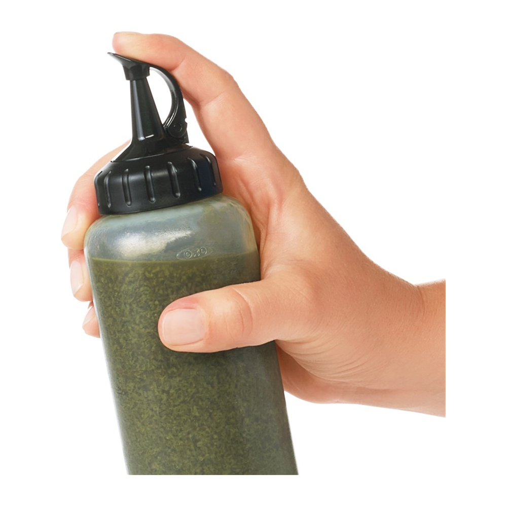 Eine Hand hält eine grüne Soßenflasche mit schwarzem Ausgießer.