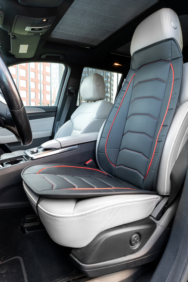 A black car seat cover with red stitching on a grey leather seat.