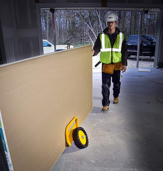 A construction worker transports drywall sheets using a hand truck on a construction site.