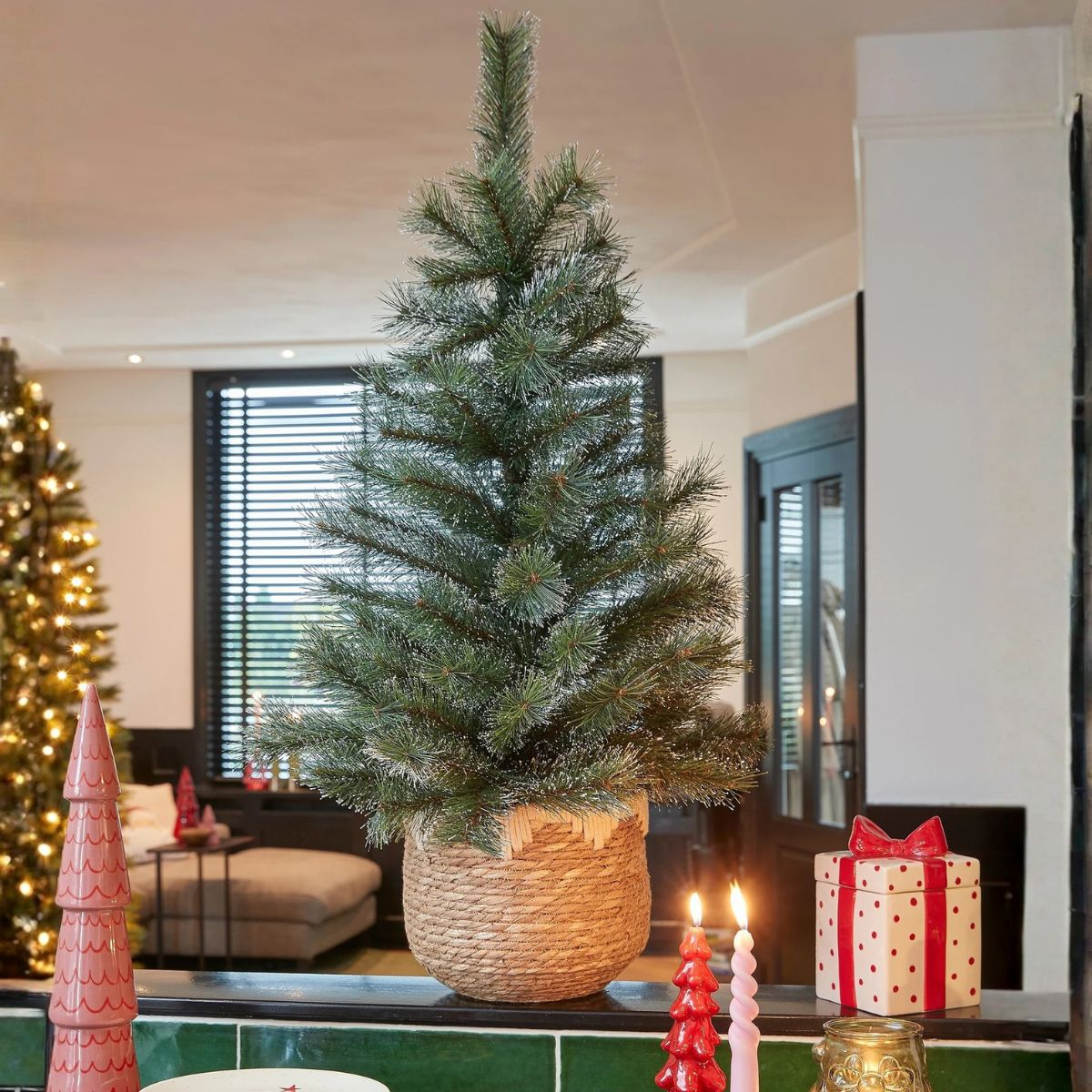 A small Christmas tree in a basket, next to candles and a gift.