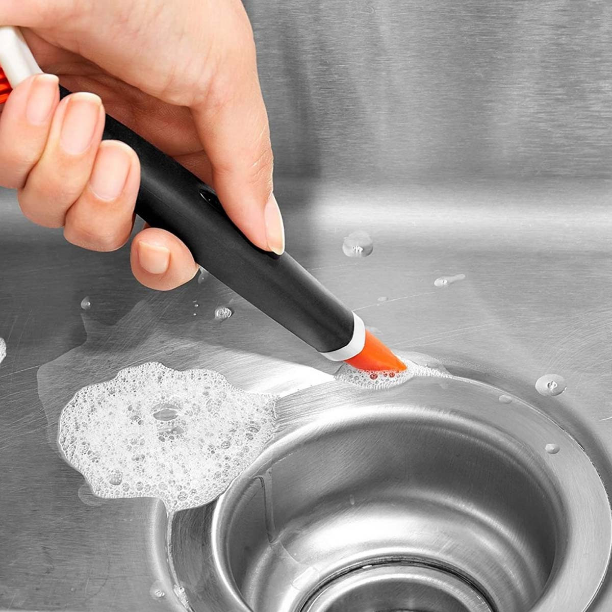 Hand reinigt Spüle mit orangefarbener Bürste und Schaum.