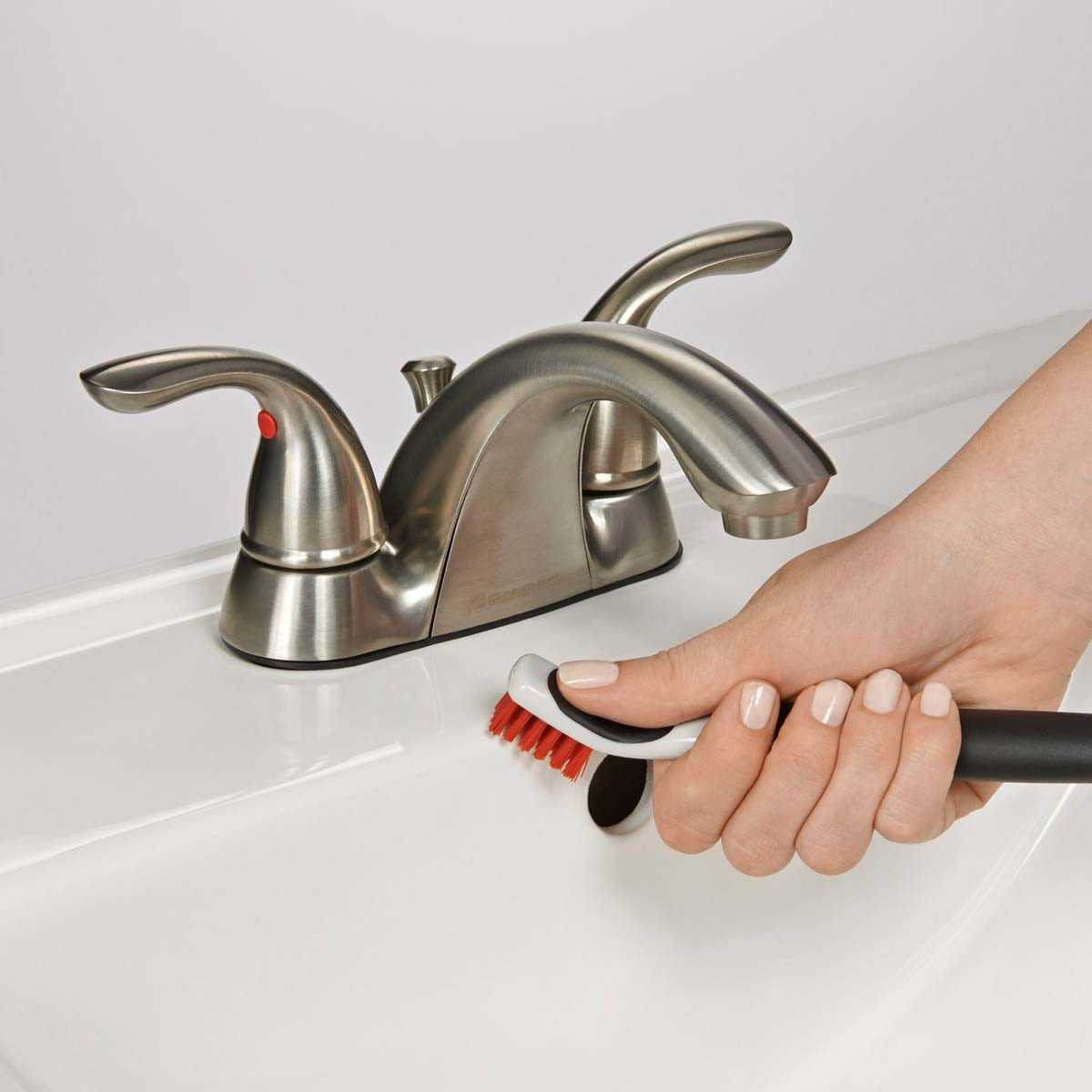 Eine Hand mit heller Maniküre reinigt ein Waschbecken mit einer Bürste.