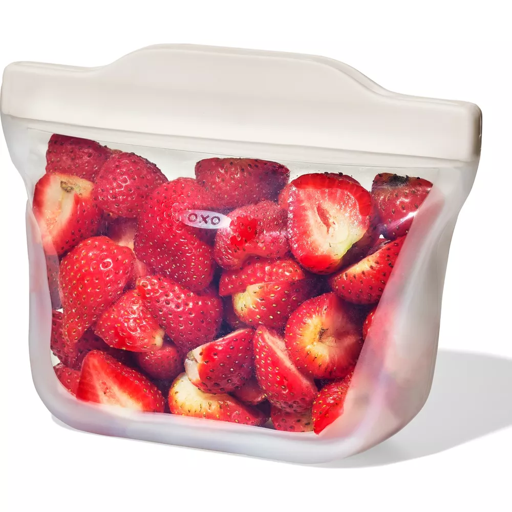Ein wiederverwendbarer Beutel voller frischer Erdbeeren, manche ganz, manche halbiert.