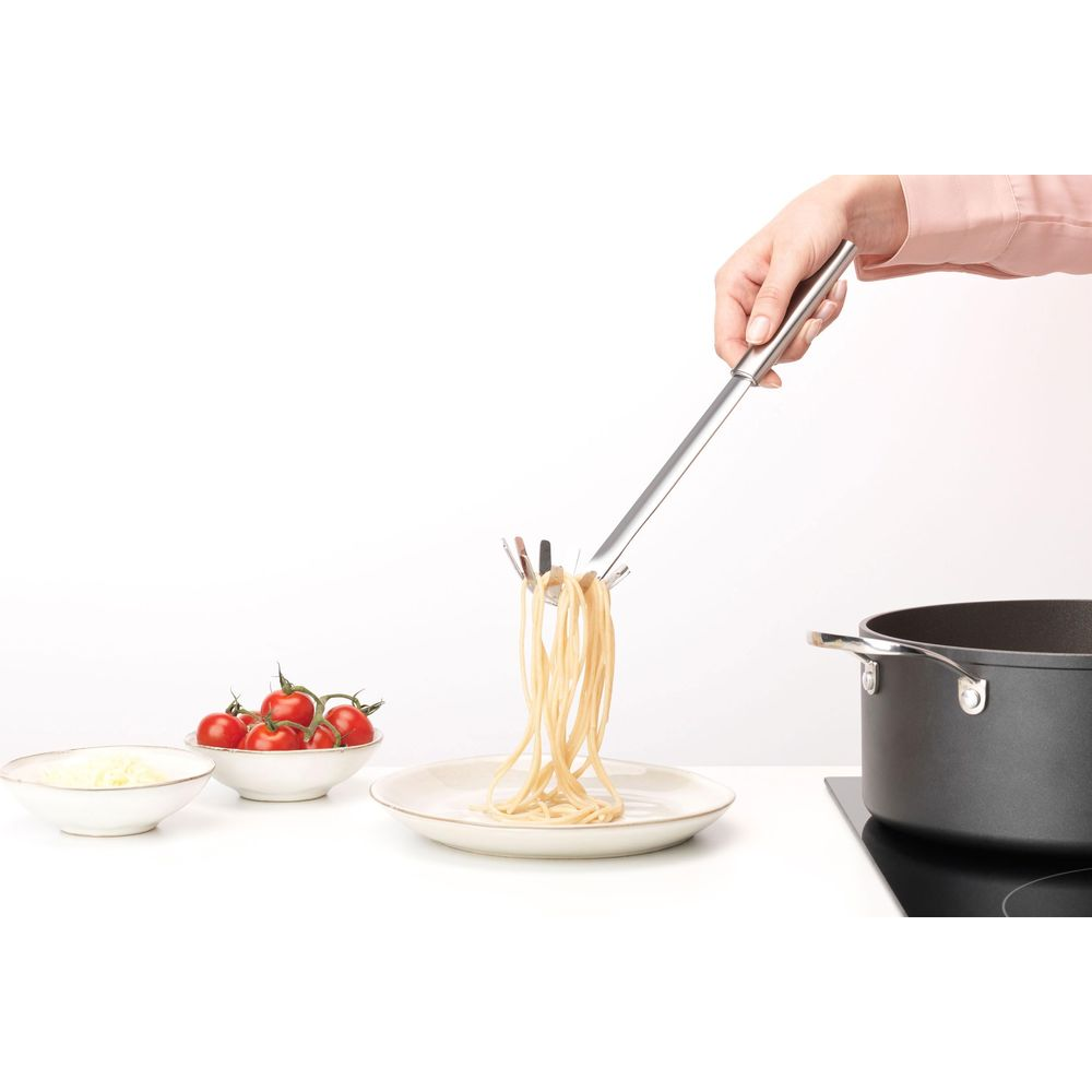 Una mano tiene un mestolo per pasta con spaghetti sopra un piatto.