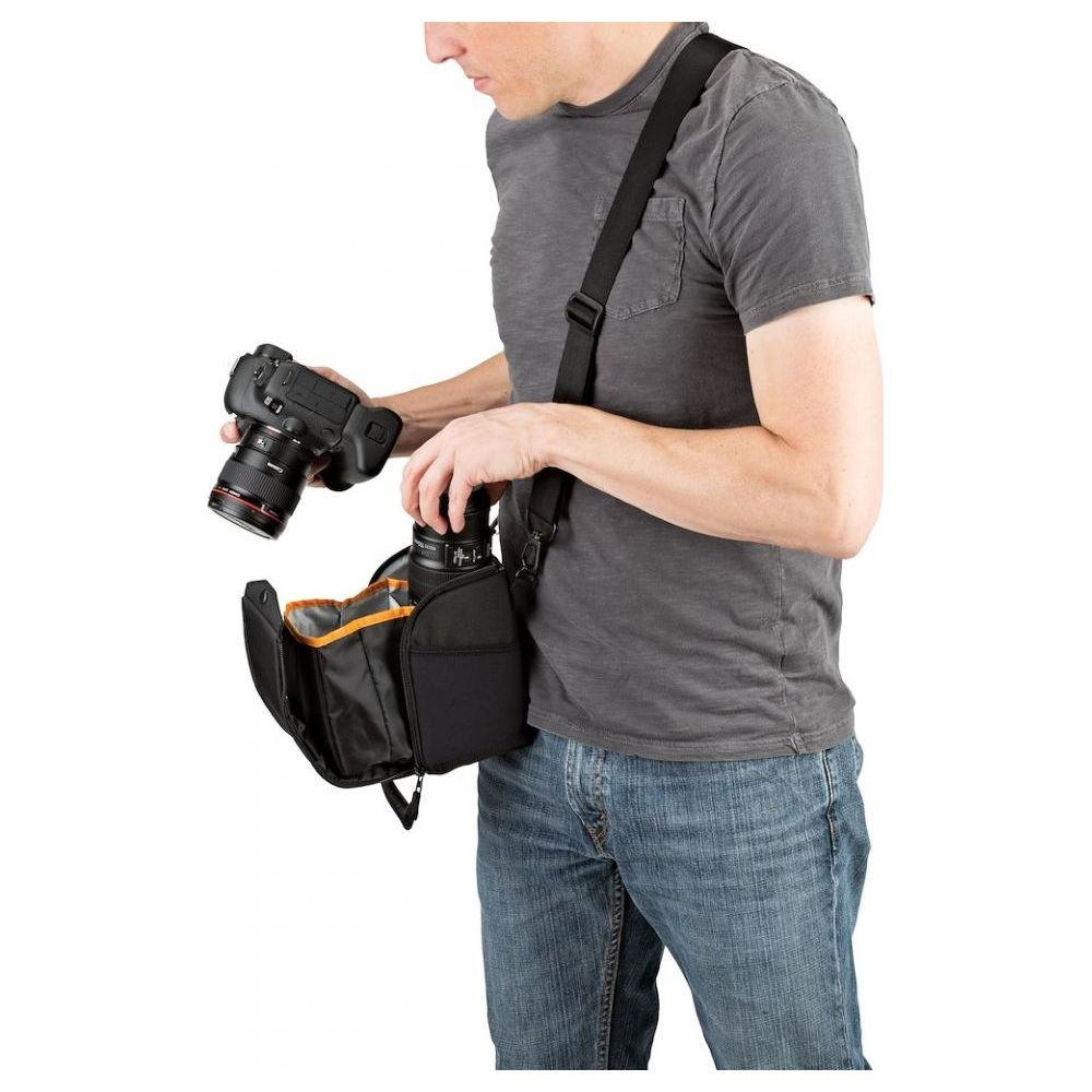 Mann in grauem T-Shirt und Jeans hält Kamera und steckt Objektiv in schwarze Tasche.